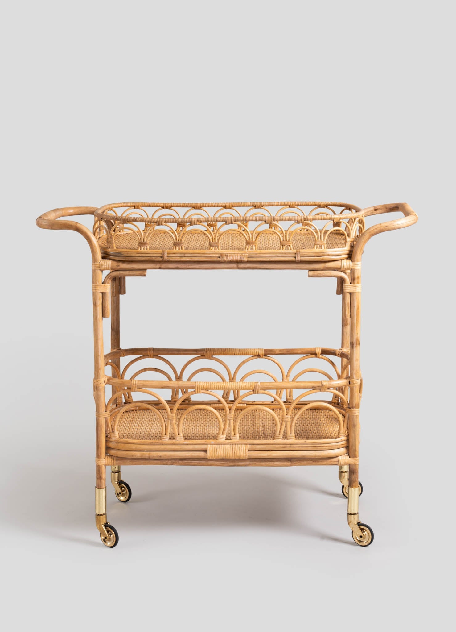 Wicker and rattan rolling bar cart with circular cutout motifs and a natural wood finish, featuring two tiers with open shelving and brass casters.