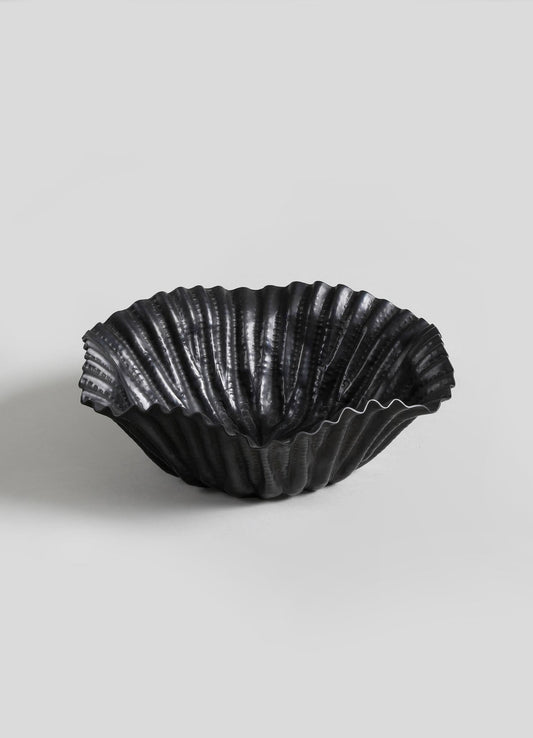A black shell-shaped dish with a textured, ribbed surface and glossy finish, made of ceramic or similar material, presented on a plain light gray background.