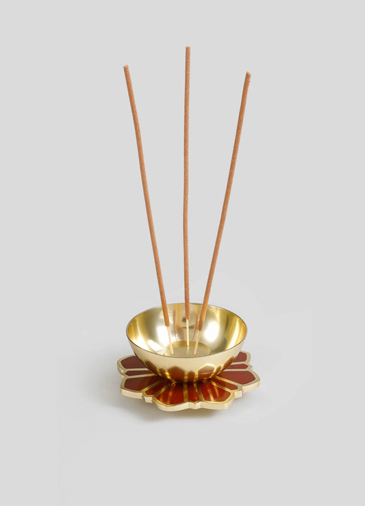 A decorative incense holder with a metallic gold bowl and a floral-shaped base in red and gold tones, designed to hold incense sticks. The holder features three upright incense sticks placed in the bowl, creating a modern and elegant aesthetic.