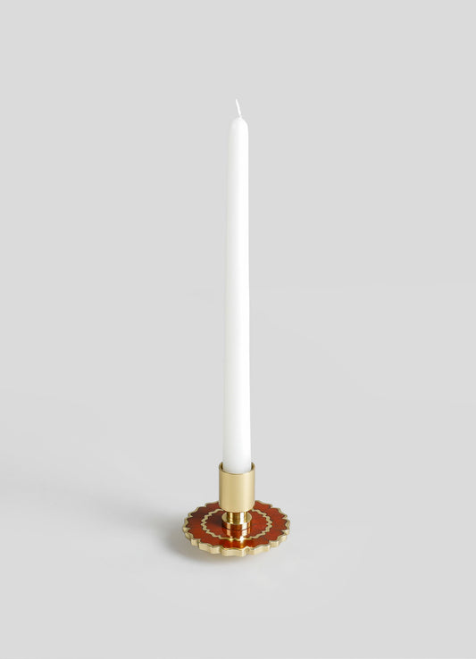 A tall white taper candle in a gold and red decorative metal candle holder with scalloped edges and geometric patterns.