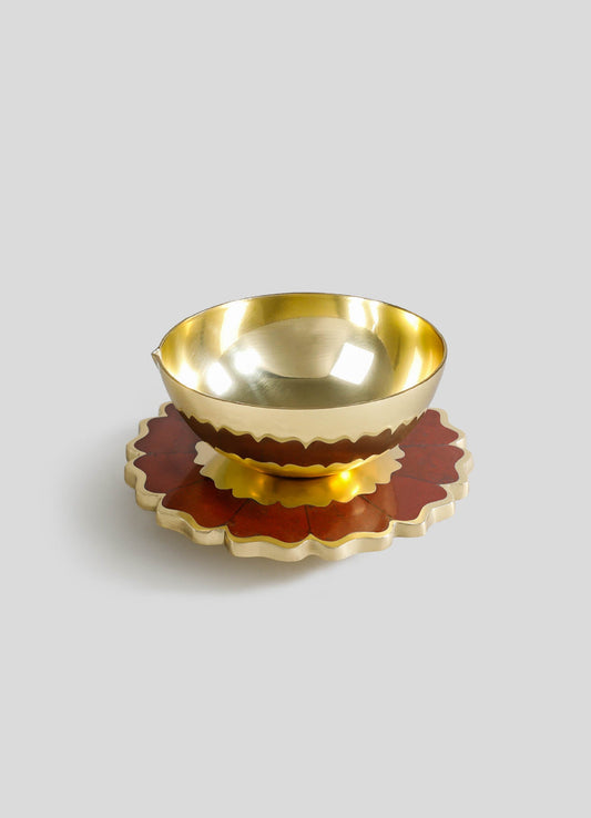 A brass bowl with a polished, reflective surface, resting on a layered scalloped base with red and gold finishes, featuring a wavy edge design.