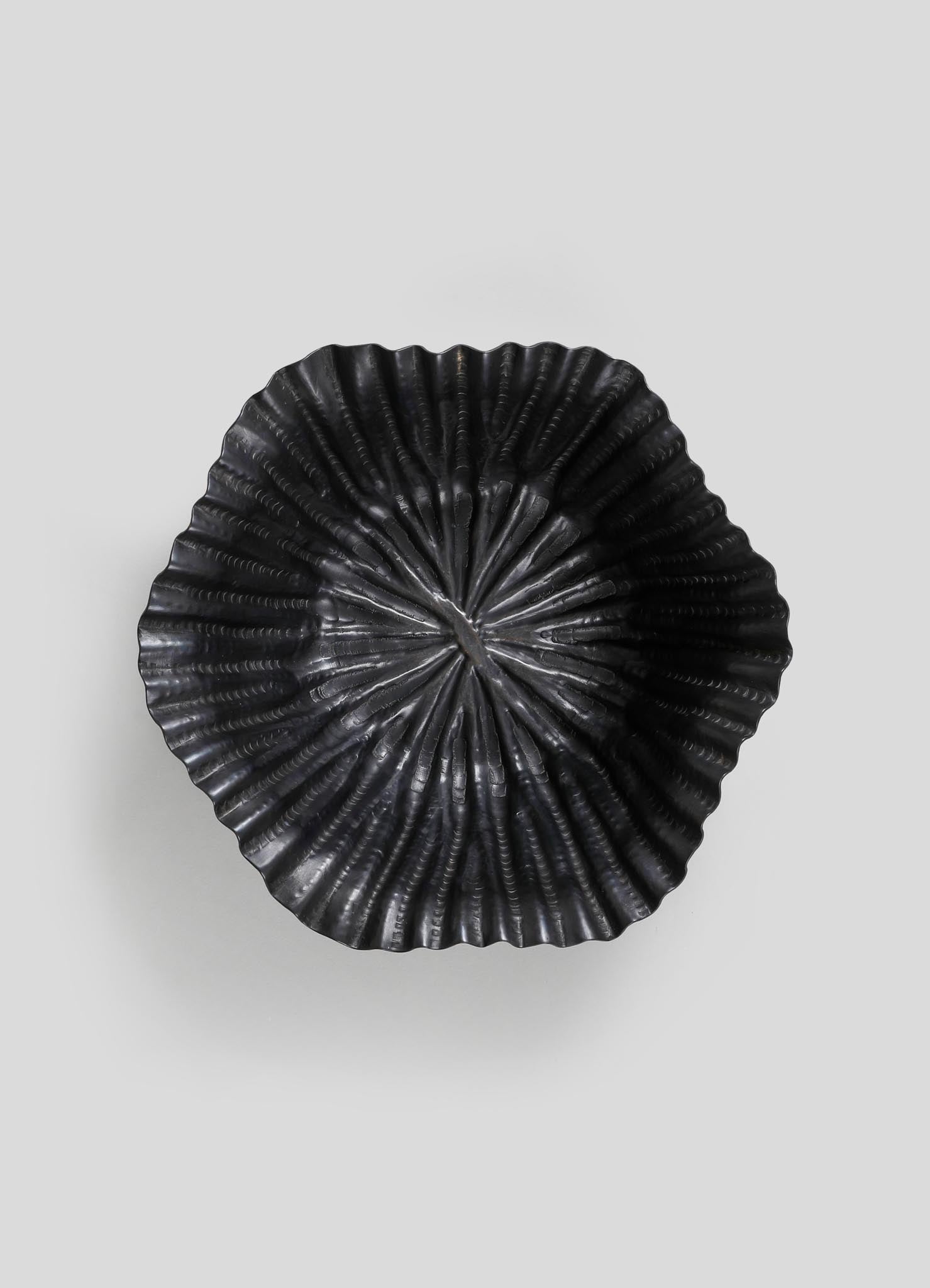 Black metal dish with a scalloped, ribbed pattern and a matte finish, featuring a circular, slightly concave shape.