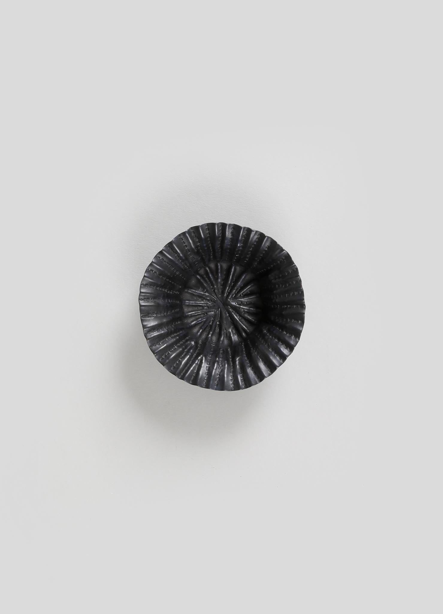 A black, ceramic bowl with a ridged, spiral pattern and a glossy finish, placed on a plain light background.