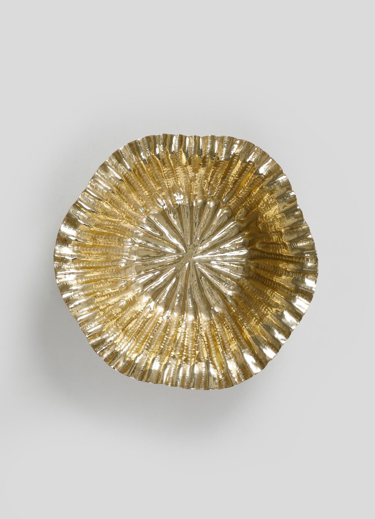A decorative bowl made of metal, featuring a ridged, fan-shaped pattern with a polished gold finish.
