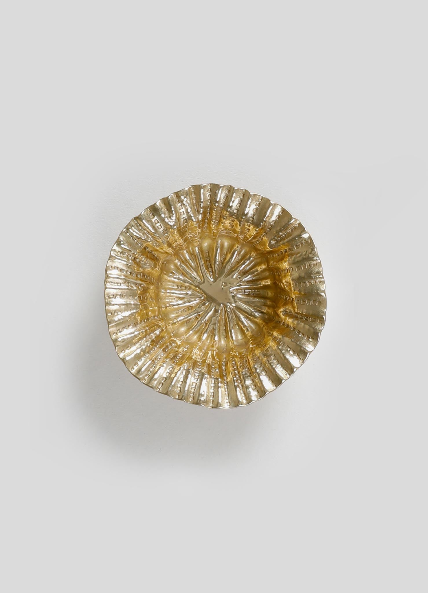 A decorative round metal dish with a ruffled, textured surface in a shiny gold finish, featuring a floral-inspired pattern with radiating ridges.