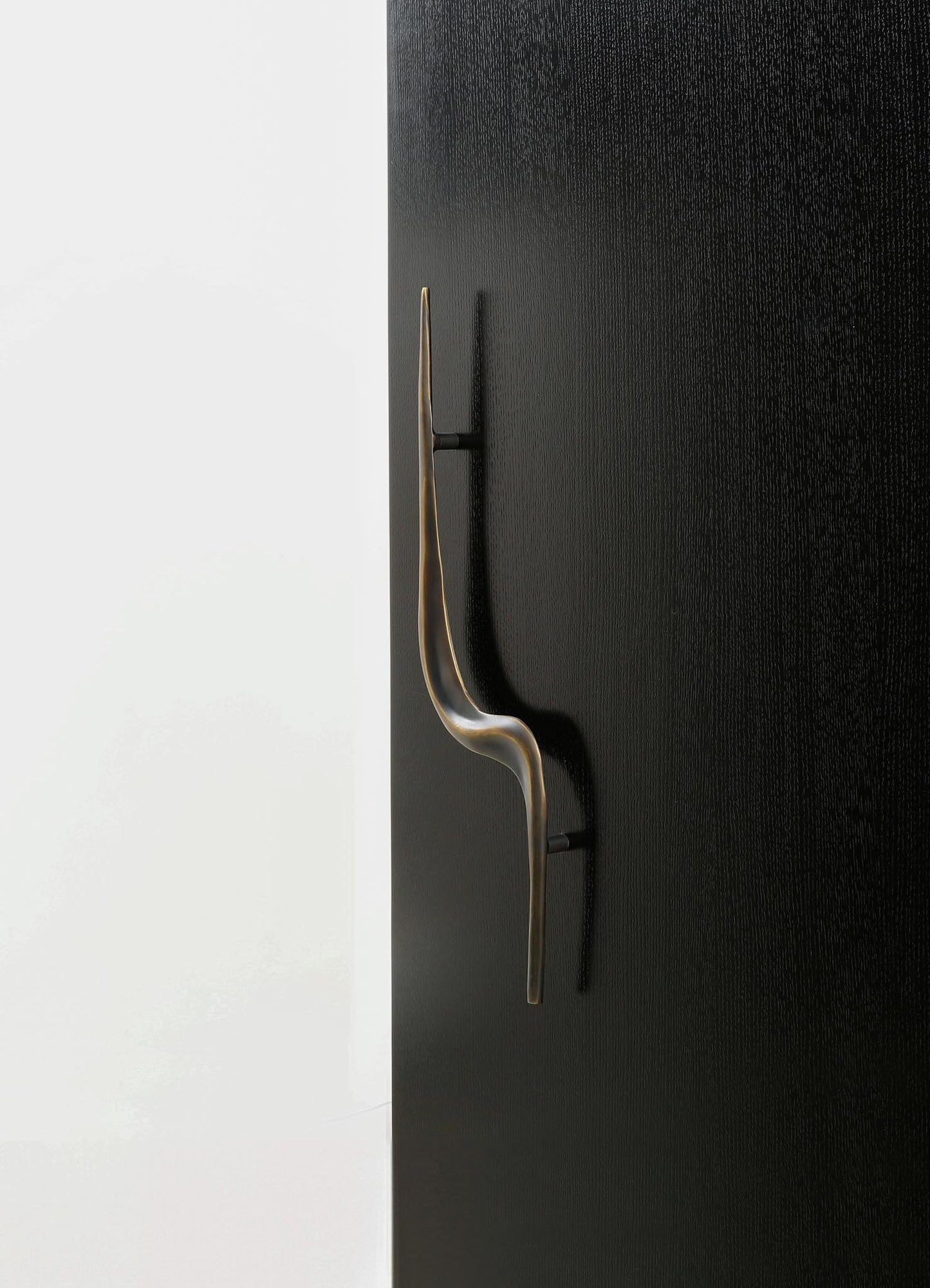 A modern black door handle with a sleek, curved design mounted on a black textured door. The handle has a metallic finish, contrasting with the matte black surface, and is positioned against a white background.