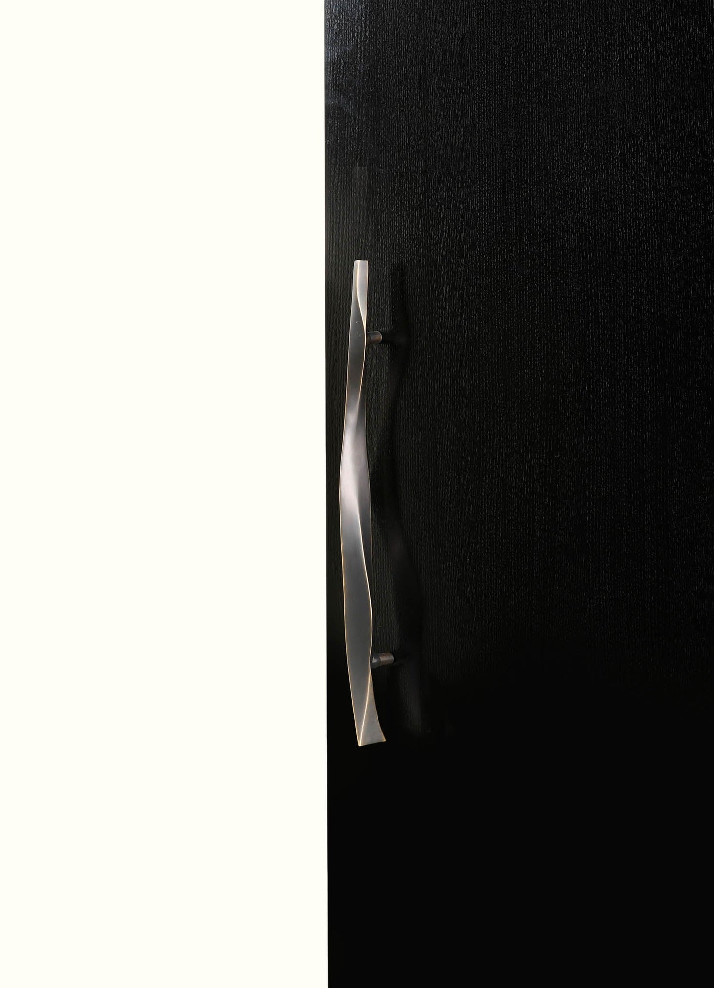 The image features a close-up of a black upholstered item, possibly a headboard or furniture piece, with a sleek, curved silver metal handle or accent on its side. The background is divided into two contrasting sections: a light, off-white or cream color on the left and a textured black surface on the right.