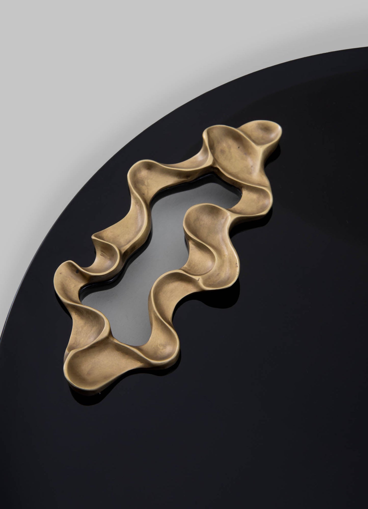 Brass decorative tray with an organic, wavy edge design, placed on a black surface with a plain background.