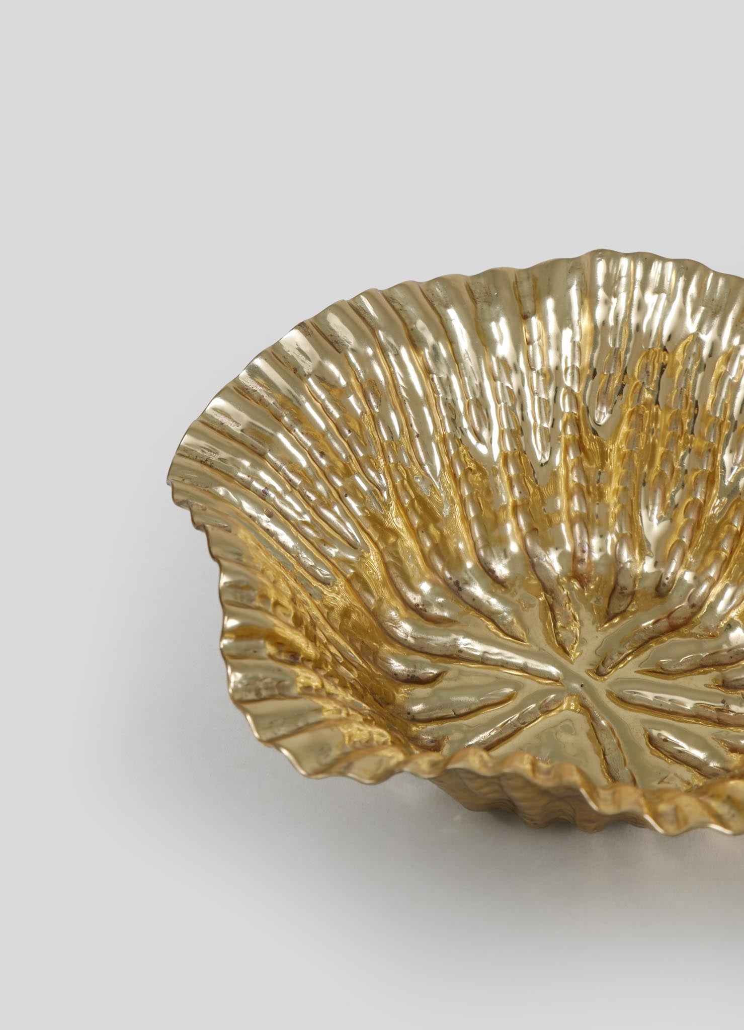 A gold metallic decorative bowl with a scalloped edge and textured, radiating lines resembling a shell or flower petal pattern. The bowl has a reflective surface with a luxurious finish, set against a plain light background.