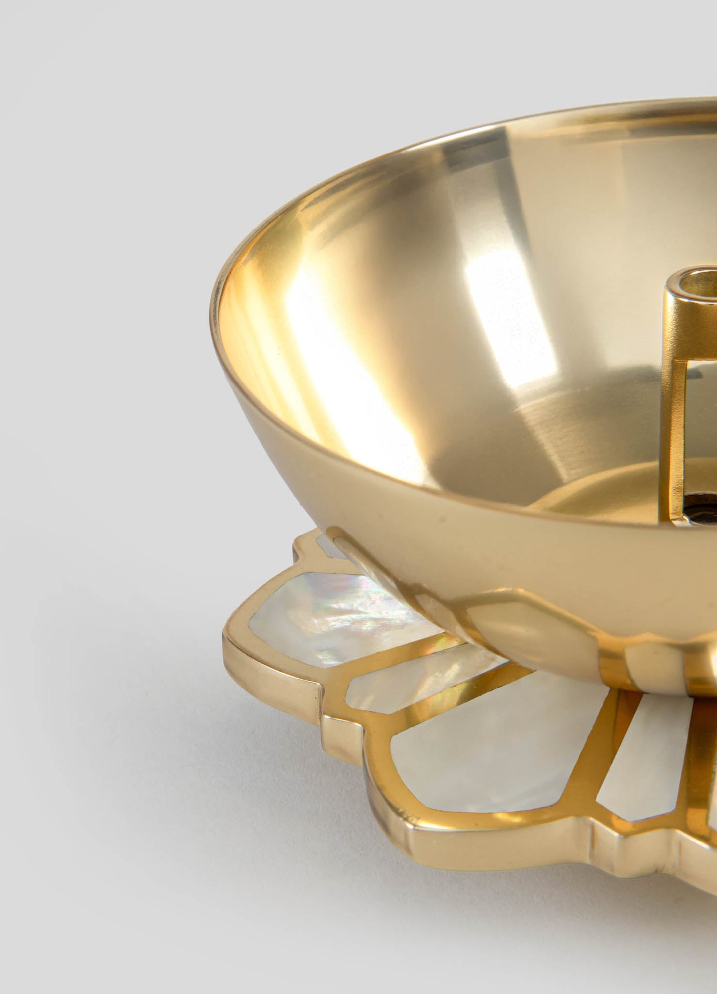 Gold-toned metal bowl with a smooth, reflective surface, resting on a decorative stand featuring cut-out geometric patterns in matching gold. The design combines contemporary elegance with a touch of decorative jewelry-inspired detailing.