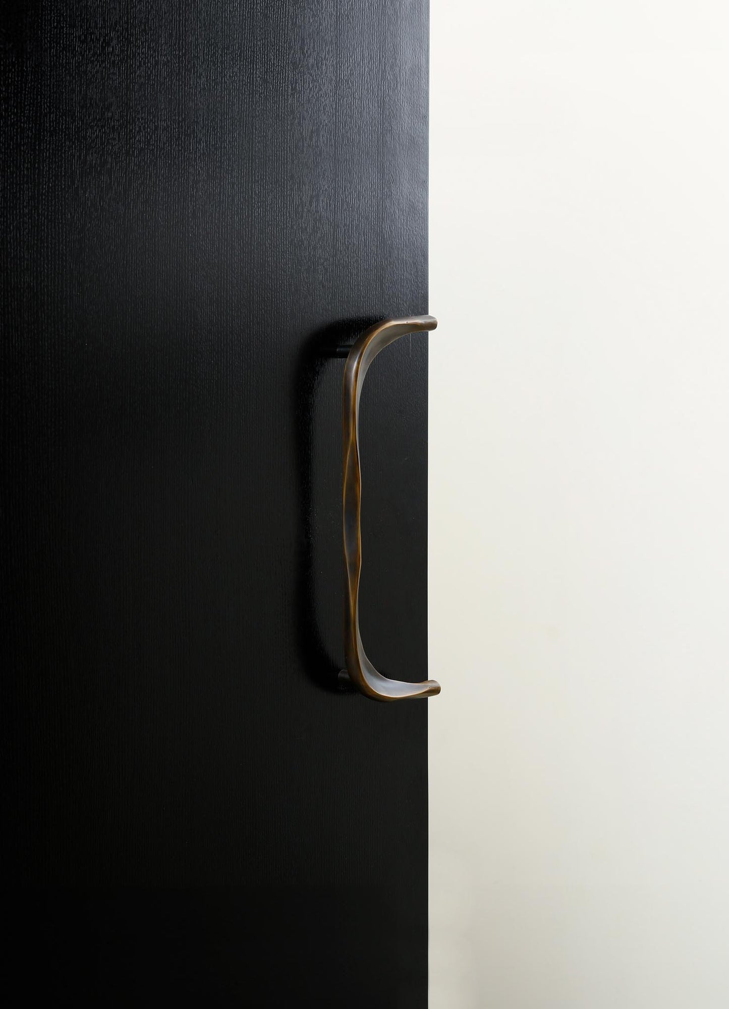 A black textured door with a brass curved handle set against a white background.