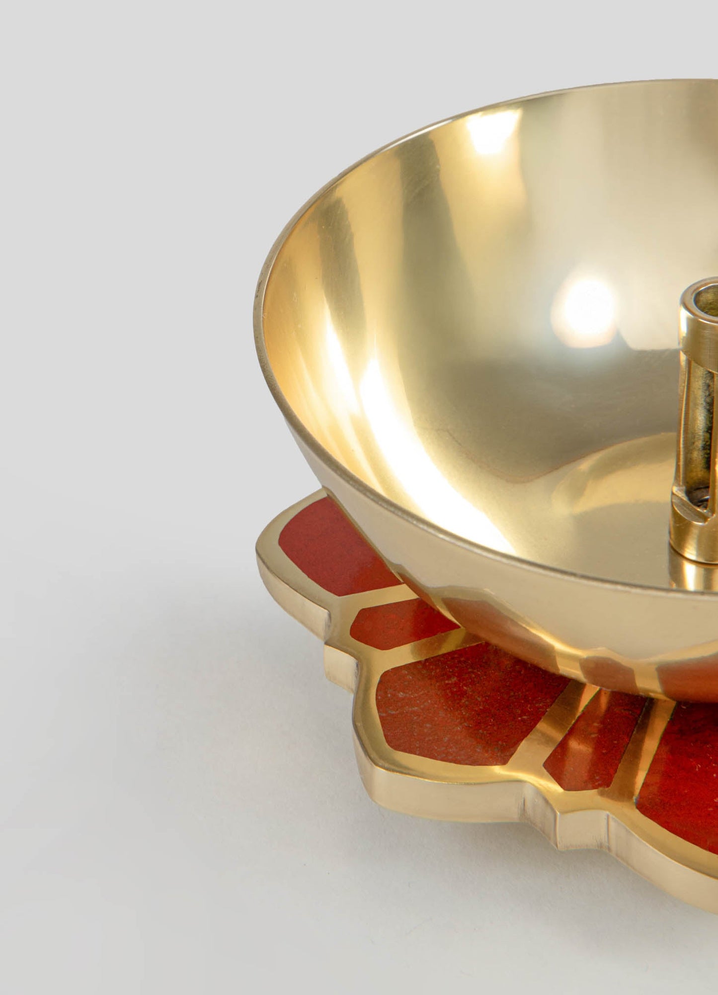 A decorative brass bowl with a smooth, reflective surface, featuring a rounded shape and a polished gold finish. It rests on a geometric-shaped base with red and gold accents, creating a contemporary and luxurious style.
