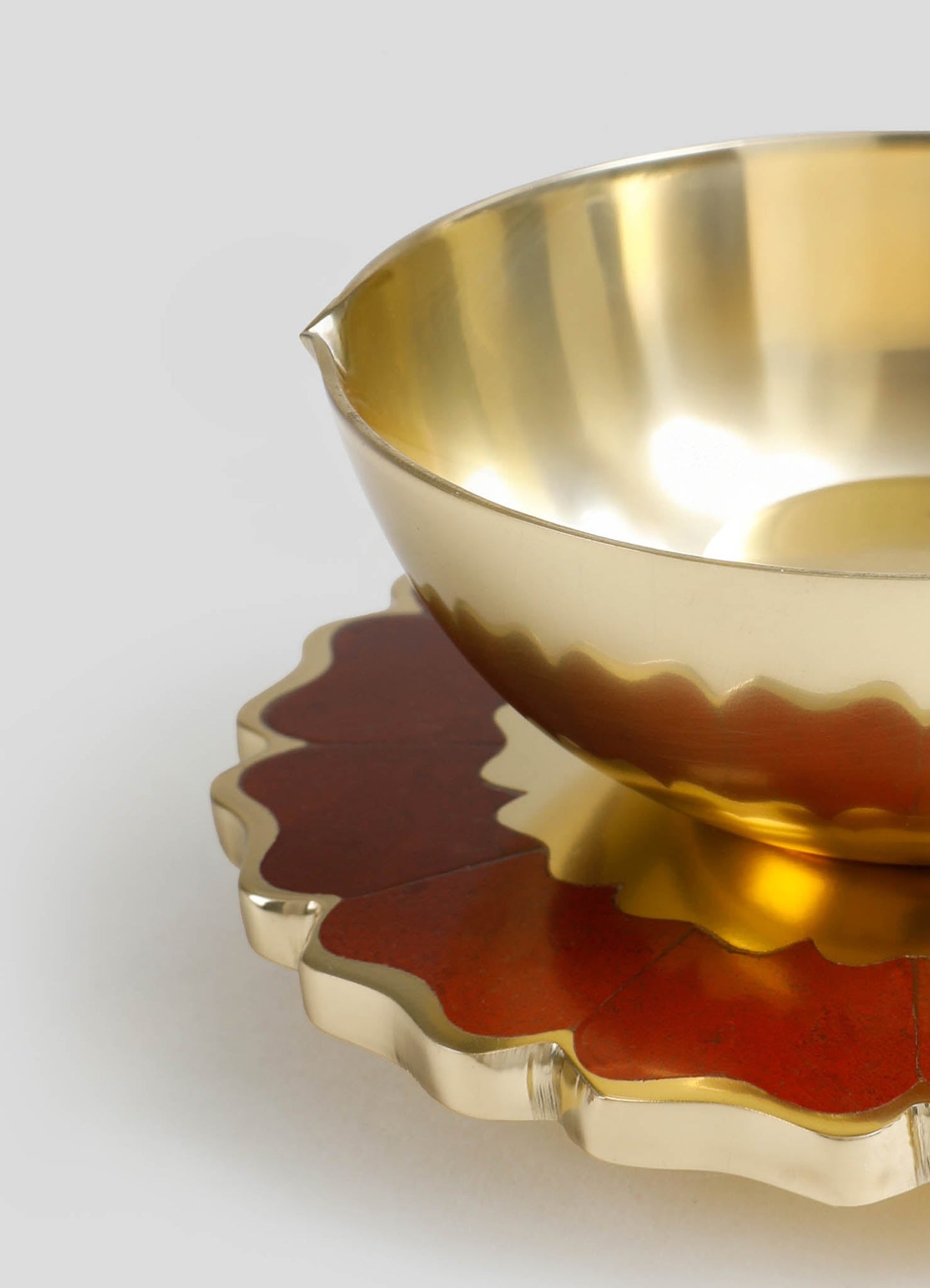 A metallic gold bowl with a smooth, shiny surface and a slightly irregular rim, placed on a decorative scalloped tray with a red and gold finish.