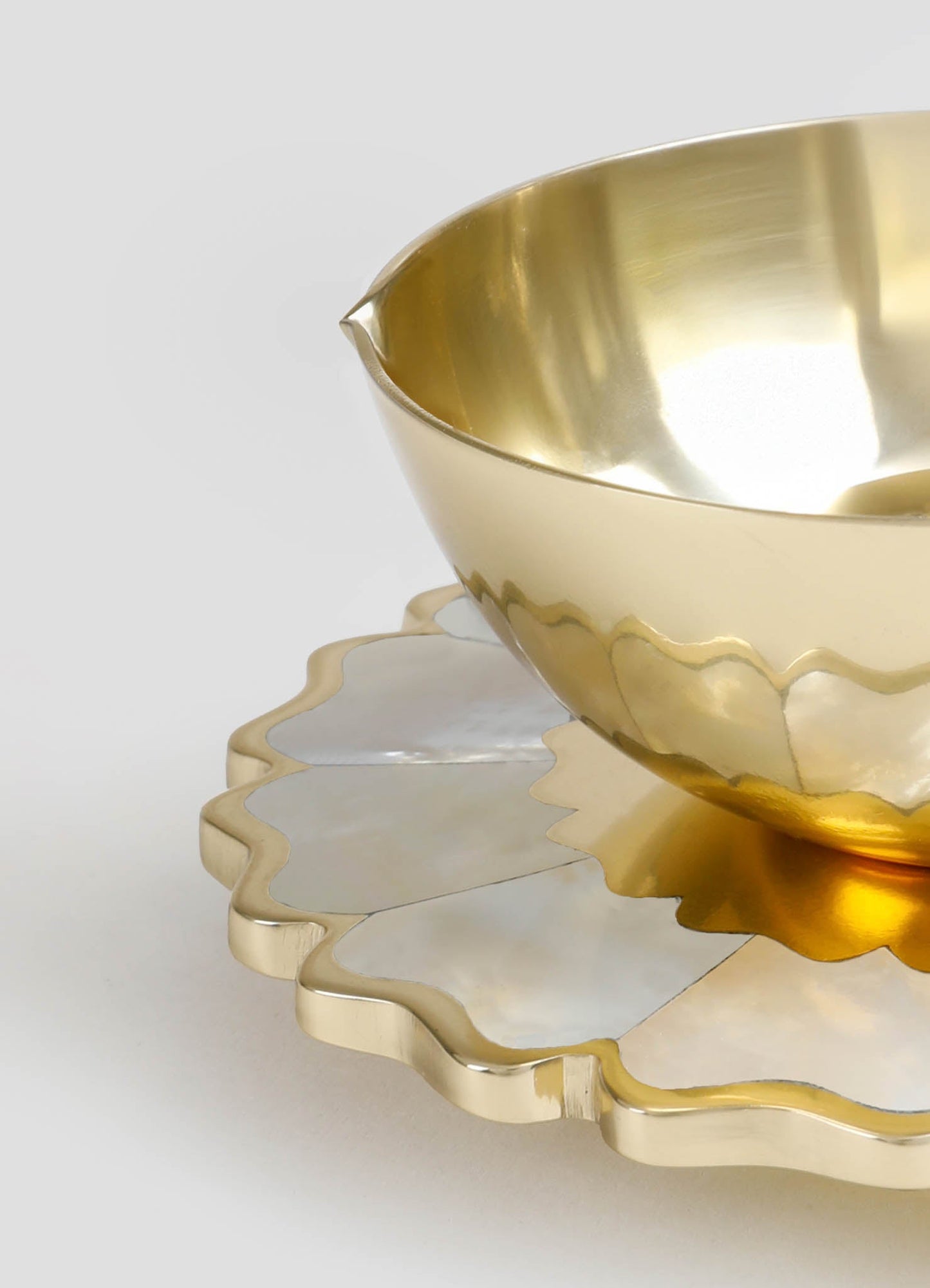 A brass bowl with a smooth, reflective surface and a polished gold finish, paired with a scalloped-edge brass tray in a similar finish. The items feature a contemporary style with sleek, minimalist design and soft metallic tones.