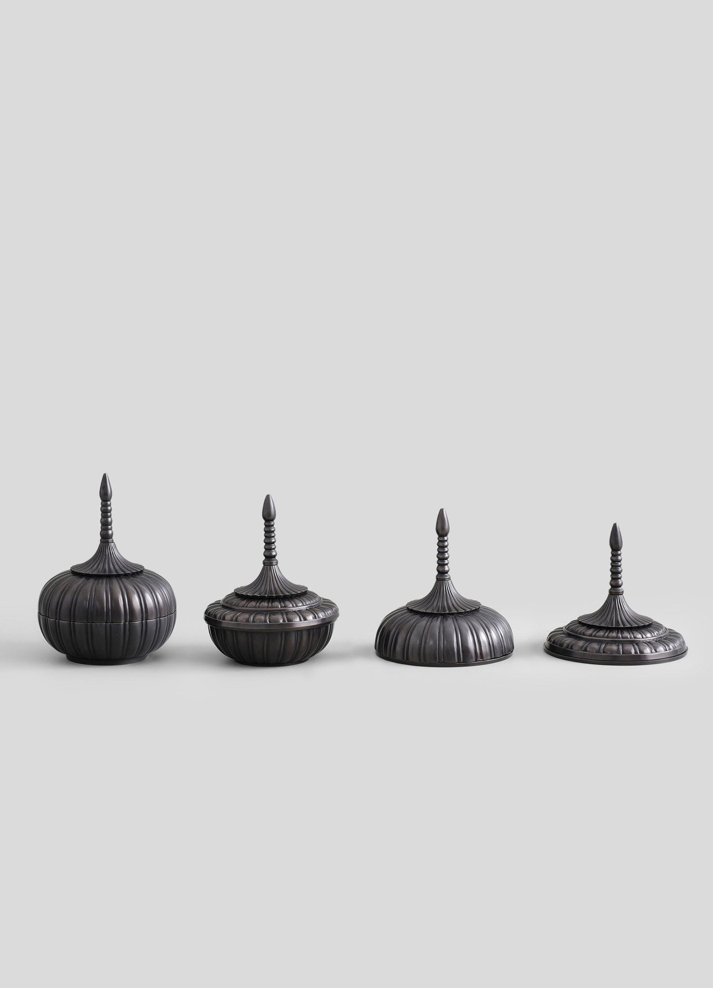 Set of four decorative metal containers with domed lids and pointed finials, finished in dark, antique bronze with ribbed and fluted detailing. They have a traditional, ornate style suitable for storage or display.