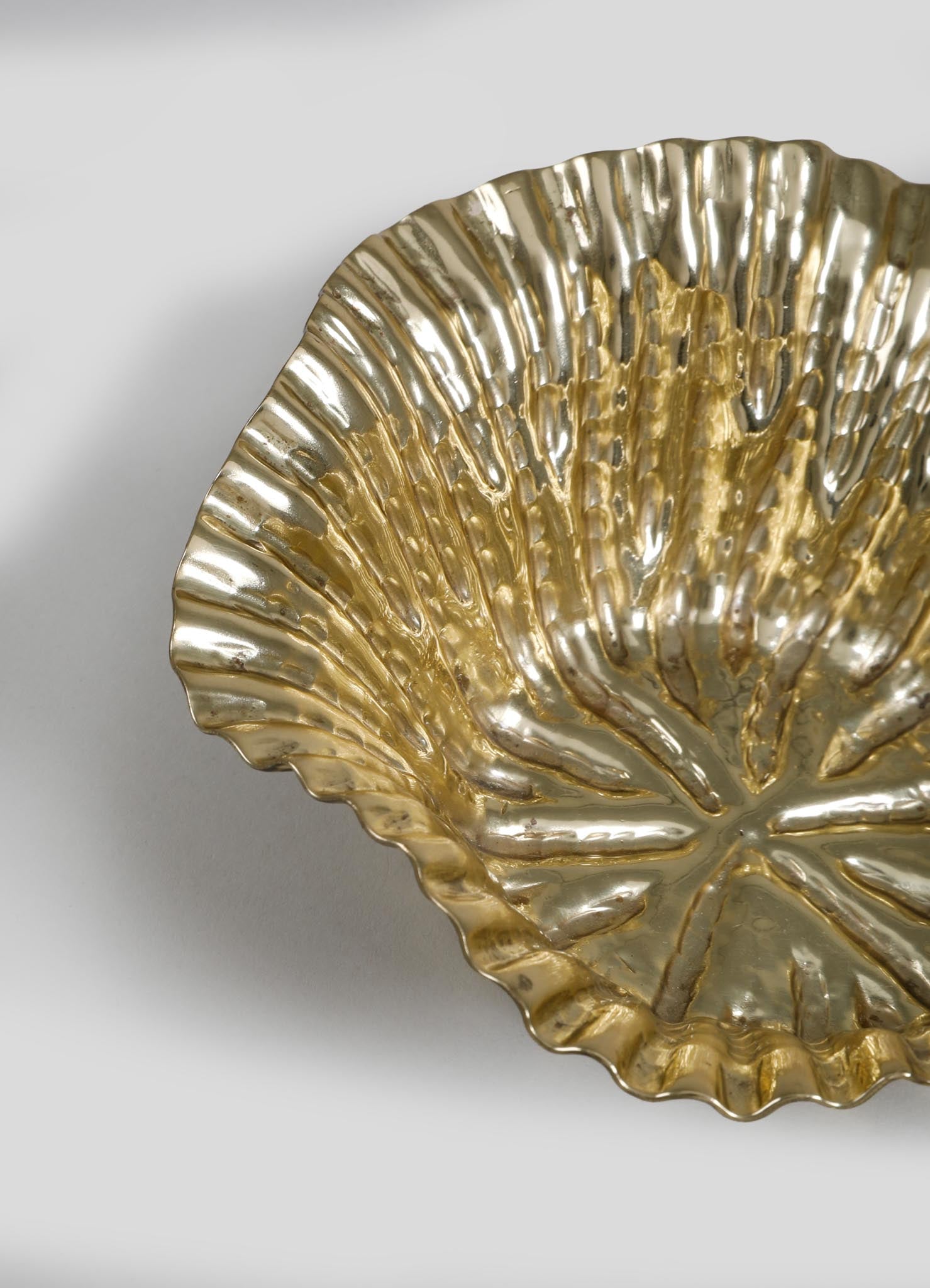 A decorative metal dish with a scalloped edge, featuring a gold-colored finish and a textured, leaf-like pattern. The dish has a reflective surface and is set against a plain background.