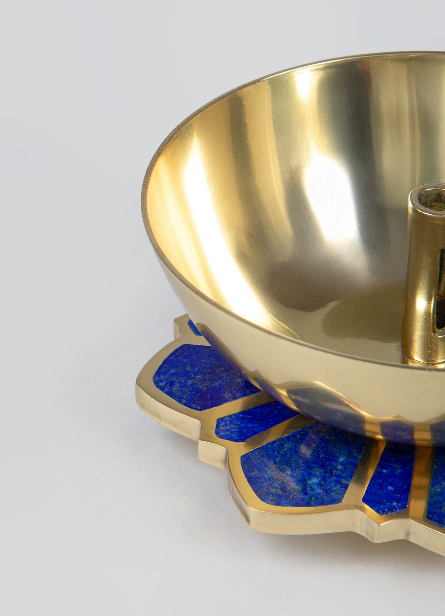 A brass bowl with a polished, reflective surface sitting on a decorative base with blue mosaic inlay and a gold-tone border. The design combines modern luxury with intricate mosaic patterns.