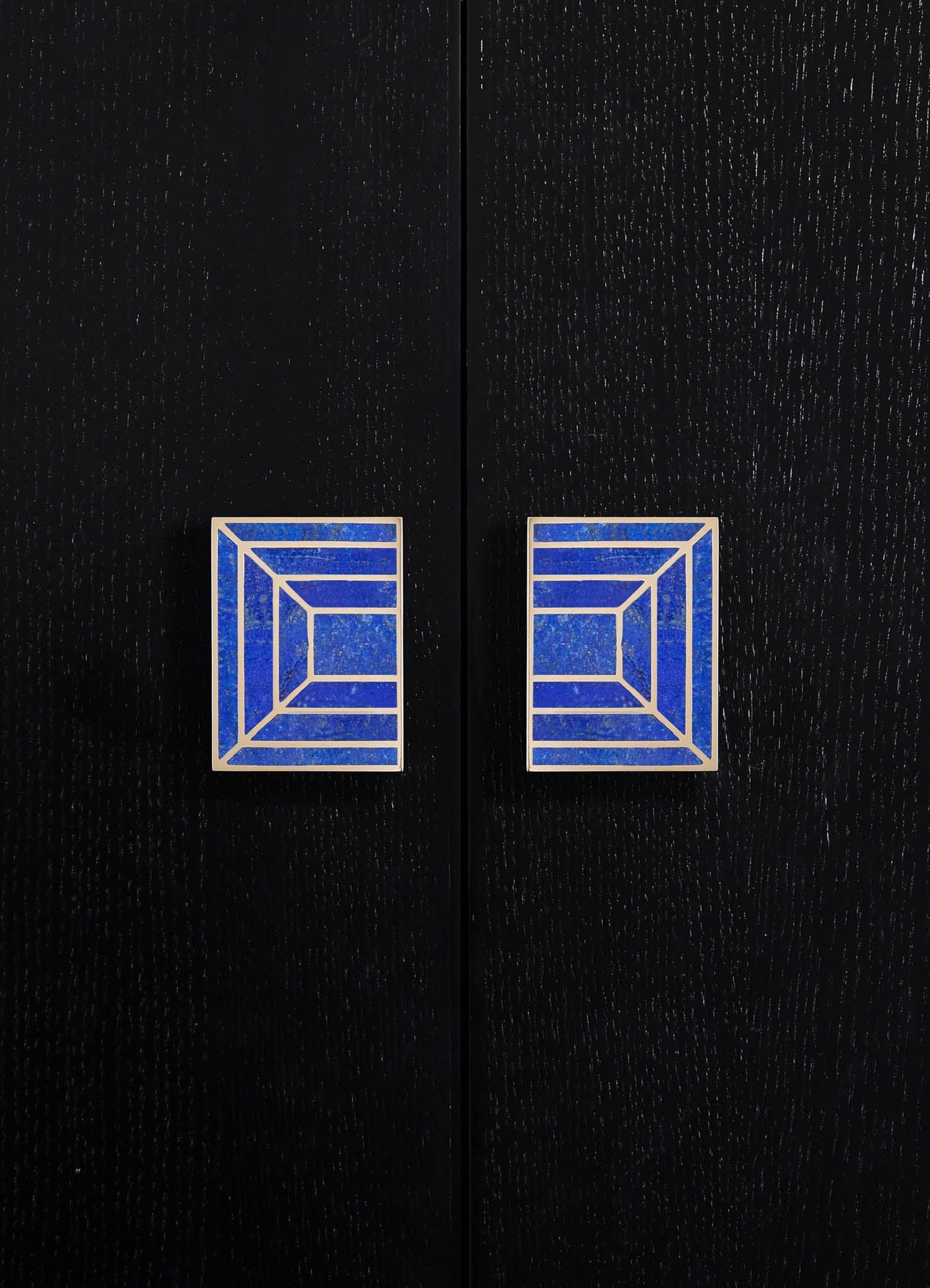 Two square cabinet handles with a geometric pattern in blue and white, mounted on a black wooden door with a textured finish.