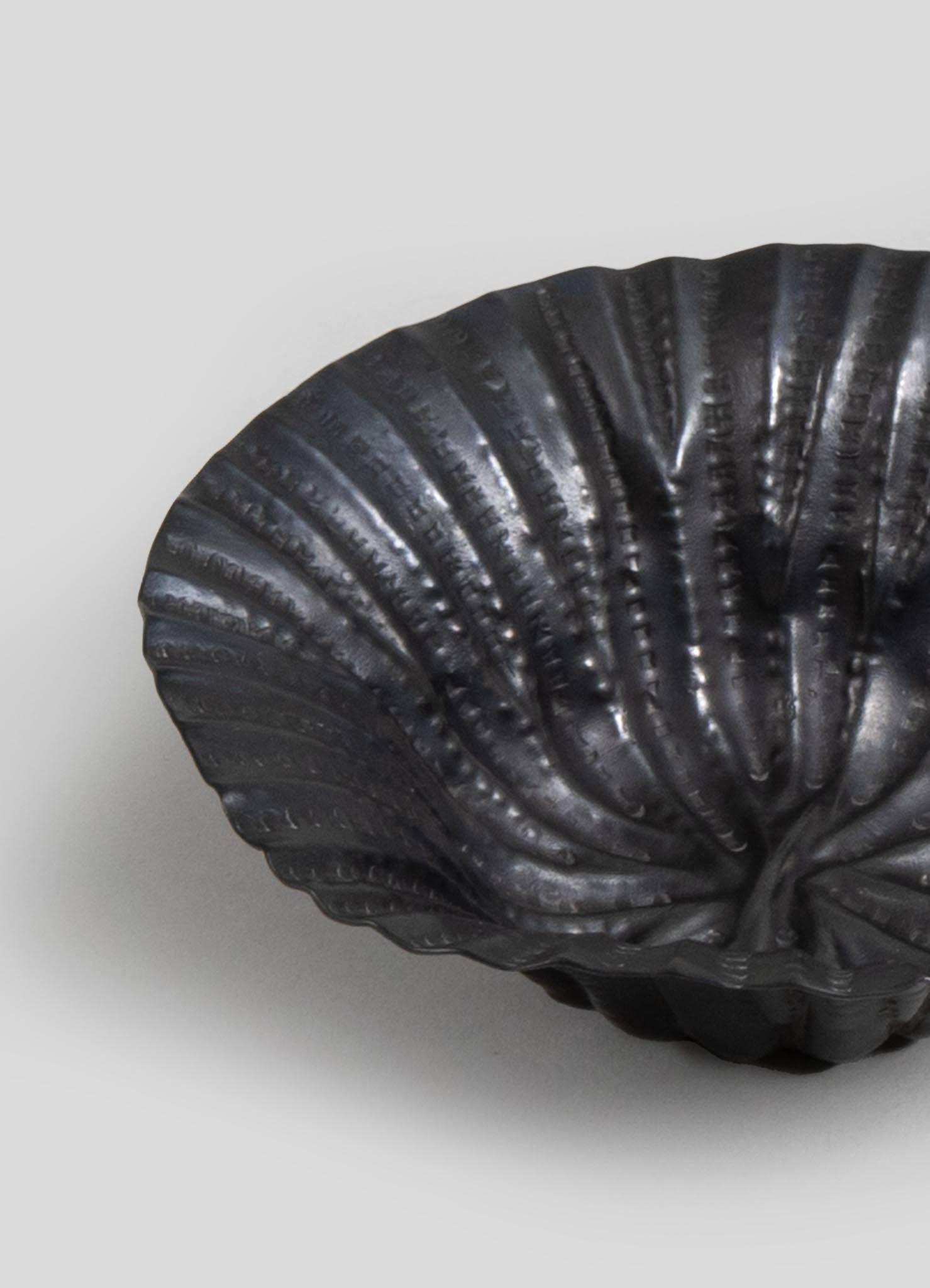 A black, shell-shaped decorative bowl with a textured, ribbed surface, made of a glossy material.