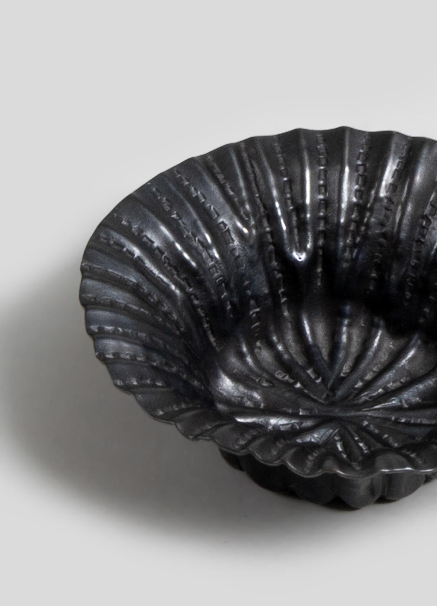 Black ceramic shell-shaped bowl with textured ridges and glossy finish, exhibiting a sculptural and decorative style.