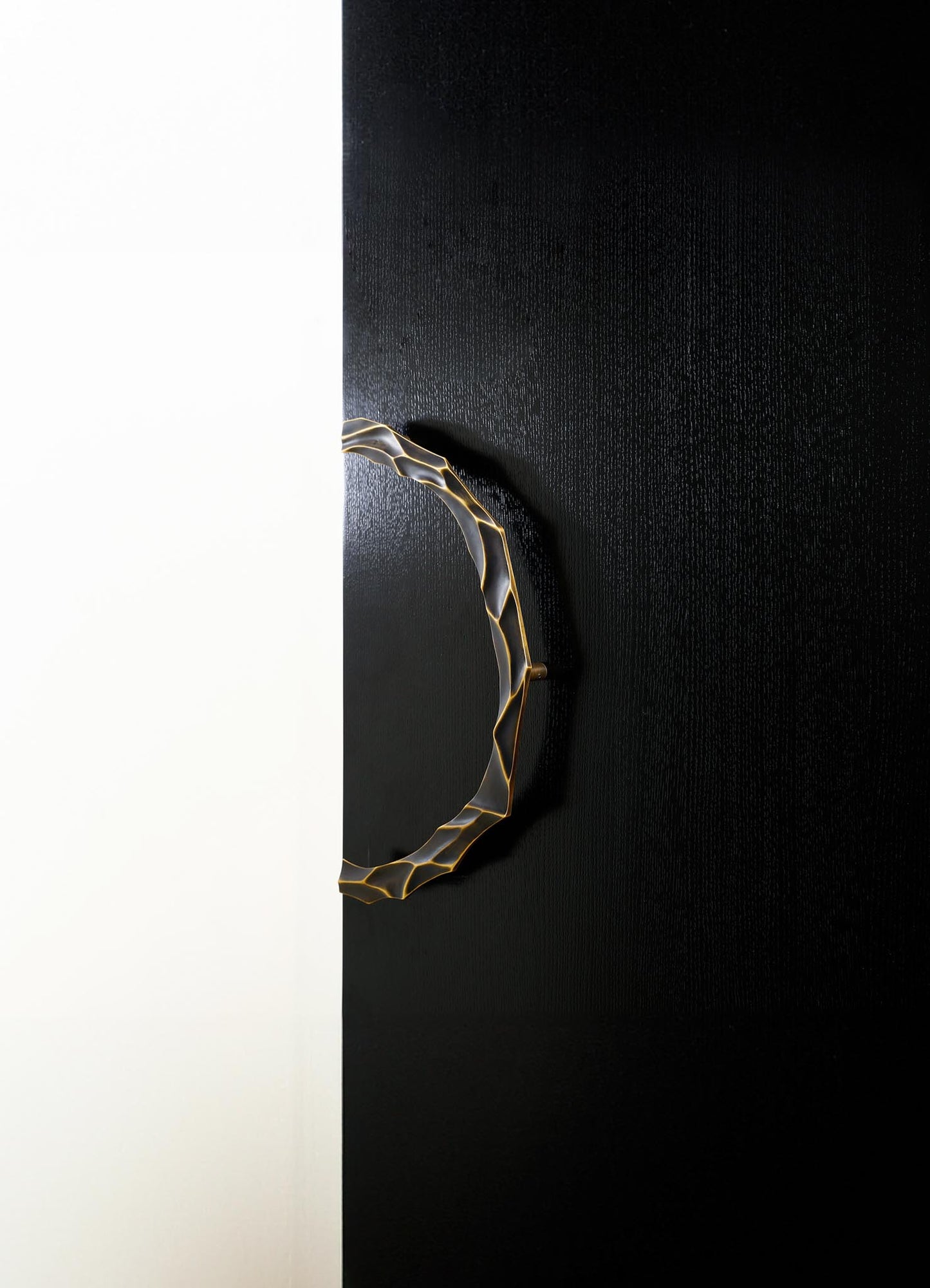 A decorative mirror with a sculptural, irregularly shaped brass frame, mounted on a black textured wall. The frame has a gold-tone finish and a distinctive organic design.