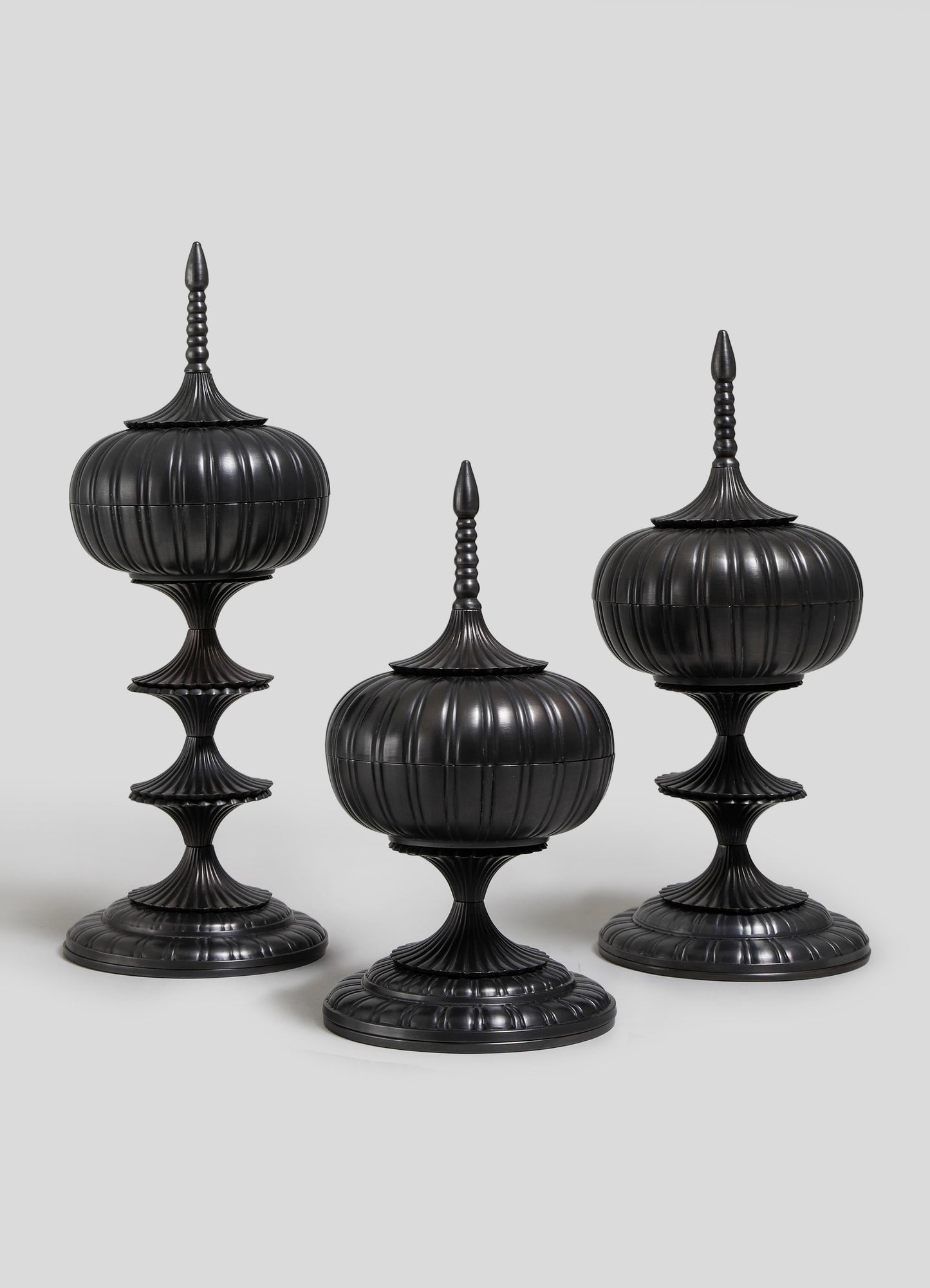 Set of three black wooden ornaments with ribbed, bulbous shapes and pointed finials, featuring layered, fluted bases and elongated, tapered tops, presented on a light gray background.