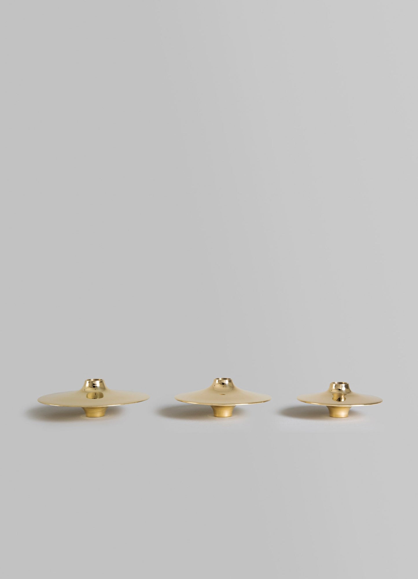 Set of three brass candle holders with wide, flat disc-shaped tops and cylindrical bases, featuring a polished metallic gold finish.
