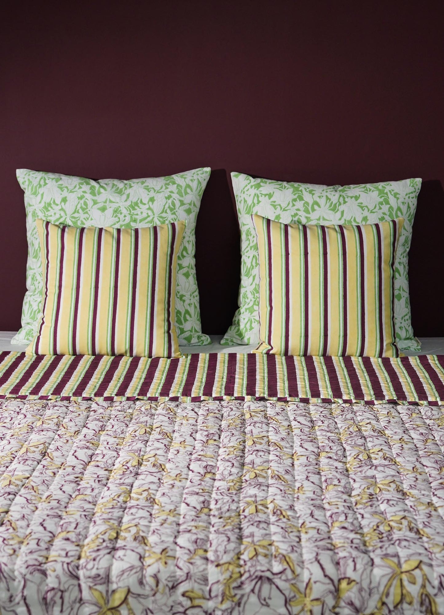 Striped pillows and floral-patterned bedspread on a bed with a dark purple wall luxury cushion cover viya green abstract
