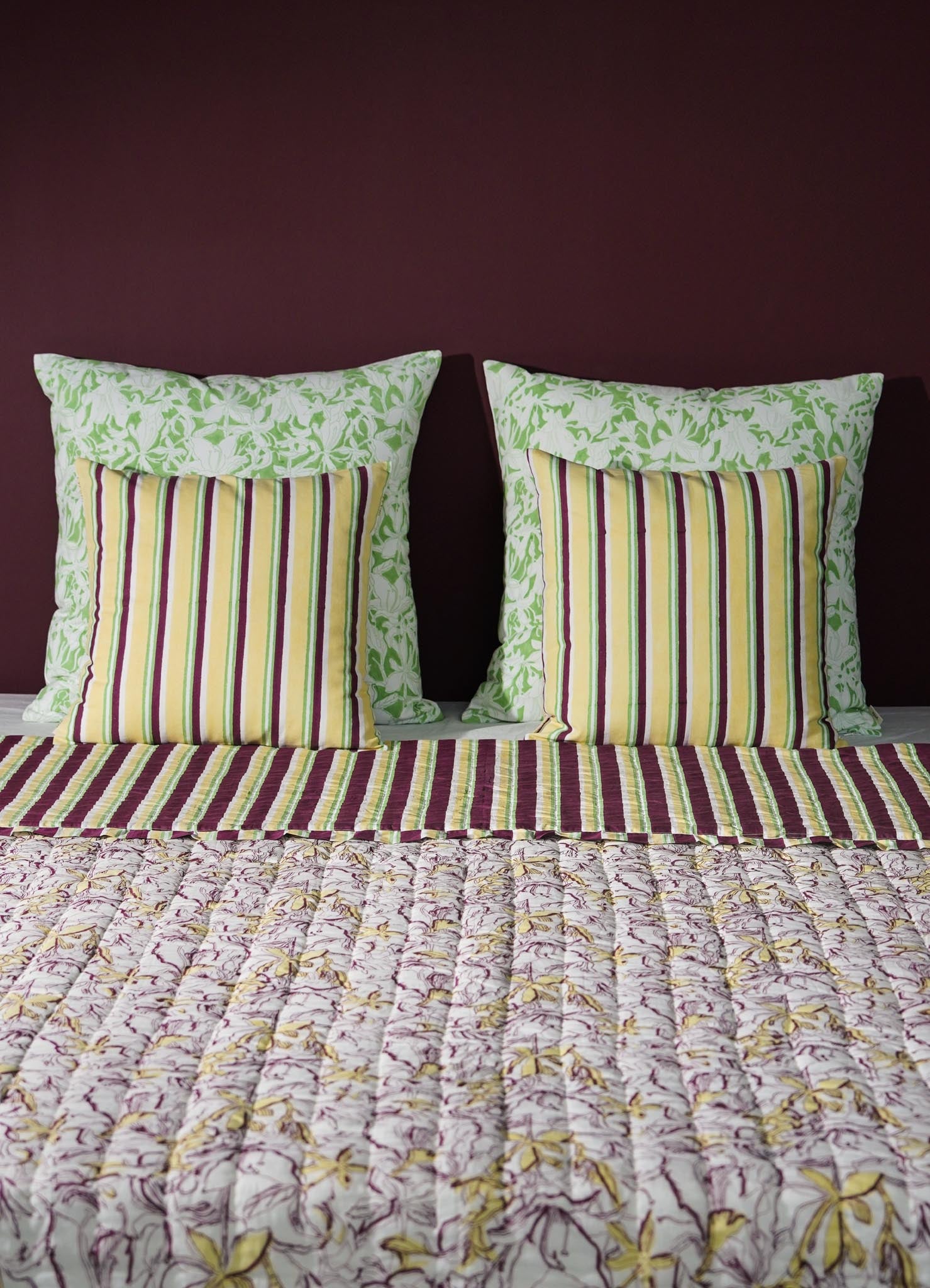 Striped pillows and floral-patterned bedspread on a bed with a dark purple wall luxury cushion cover viya green abstract