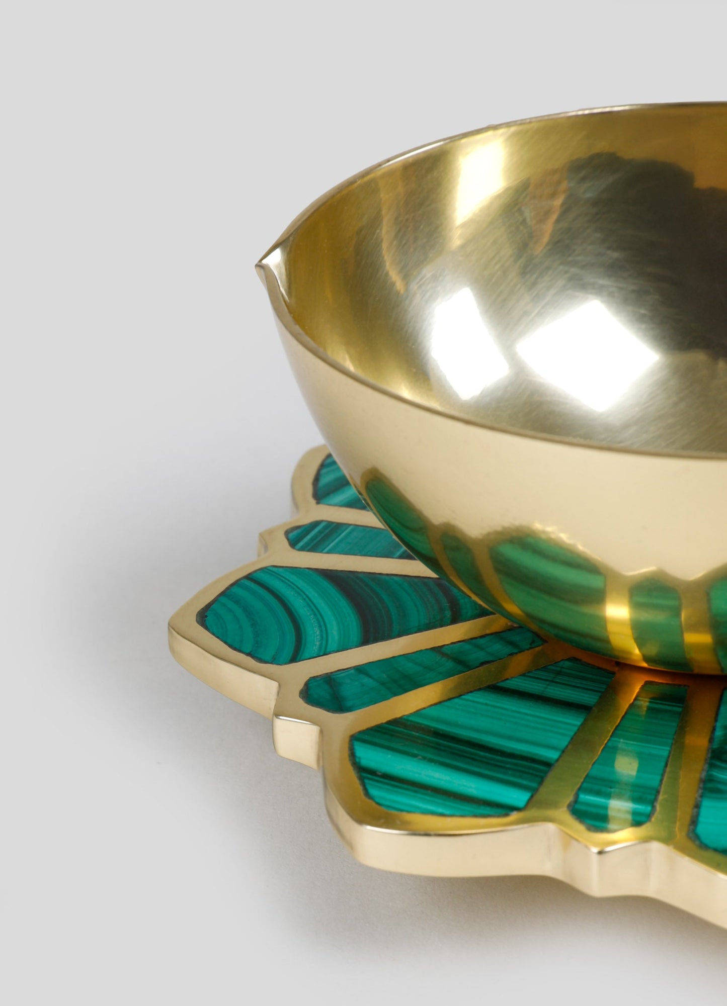 A decorative brass bowl with a polished gold interior, resting on a geometric base made of turquoise malachite inlay with gold accents, featuring a petal-like shape.