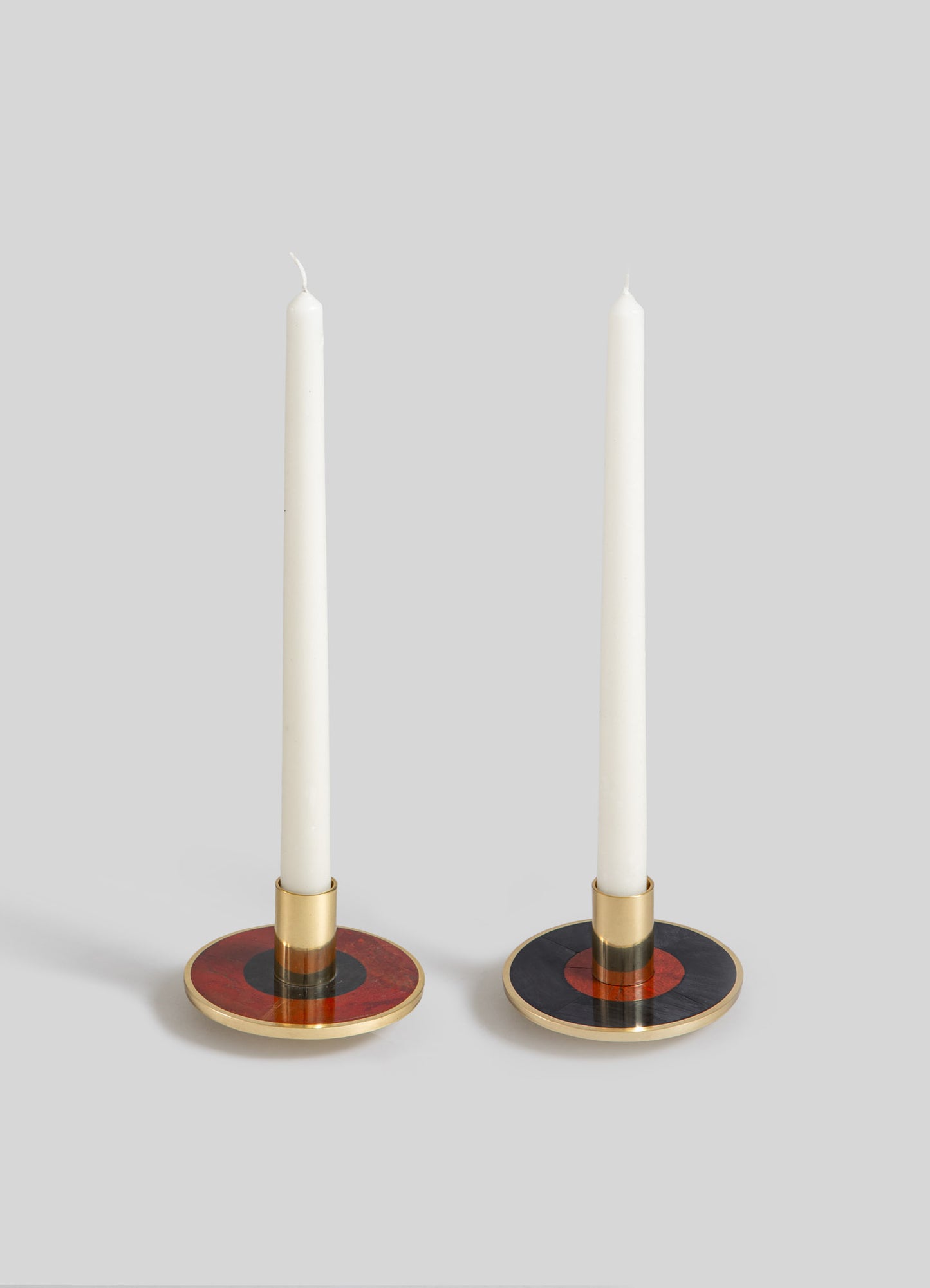 Pair of candlesticks with circular bases featuring black, red, and gold accents, and metallic gold holders, holding tall white taper candles.