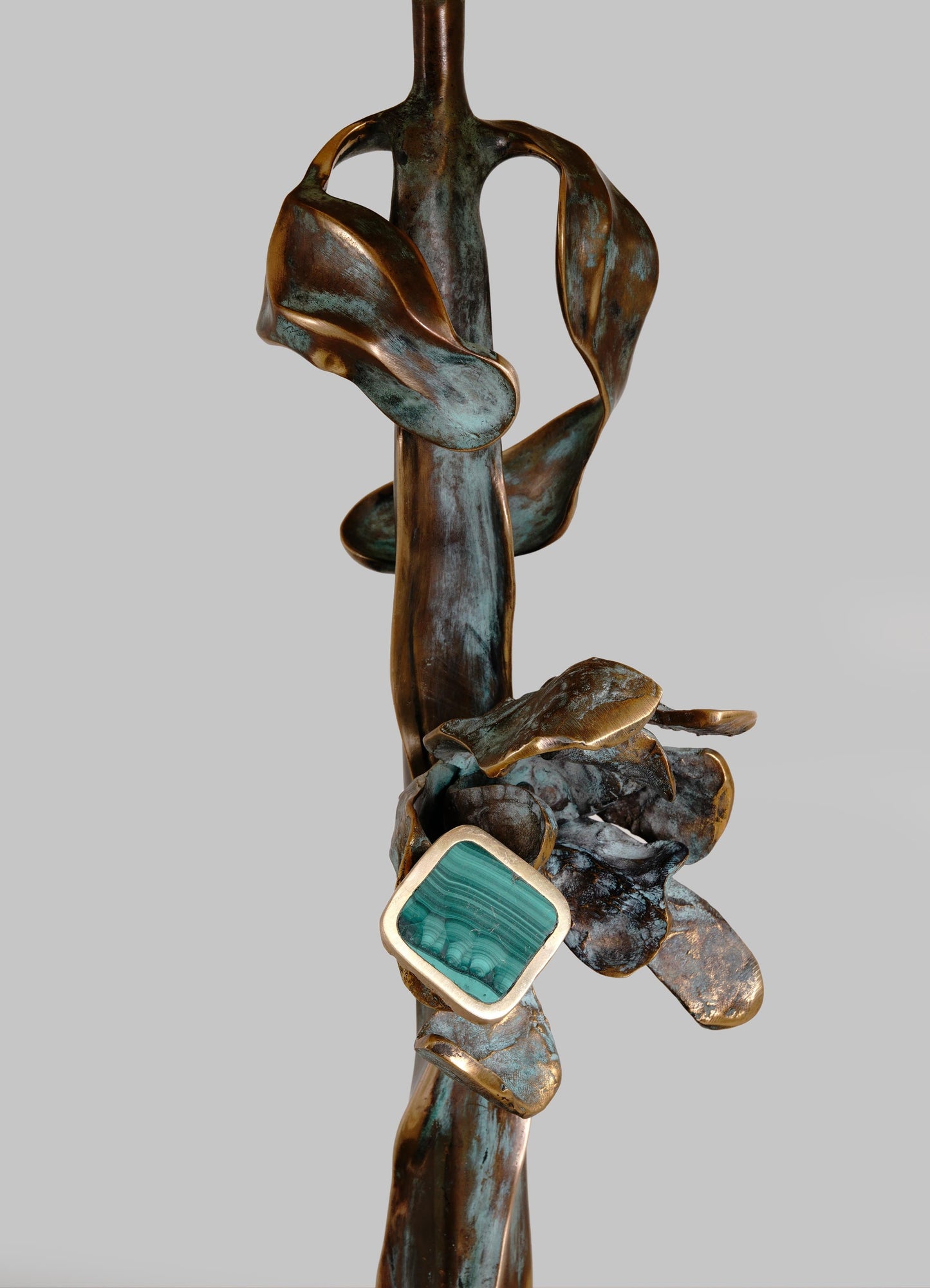 A sculptural art piece crafted from metal with a patinated finish in shades of bronze and turquoise. The design features abstract, organic shapes with a square blue-green gemstone accent set in a metallic frame.