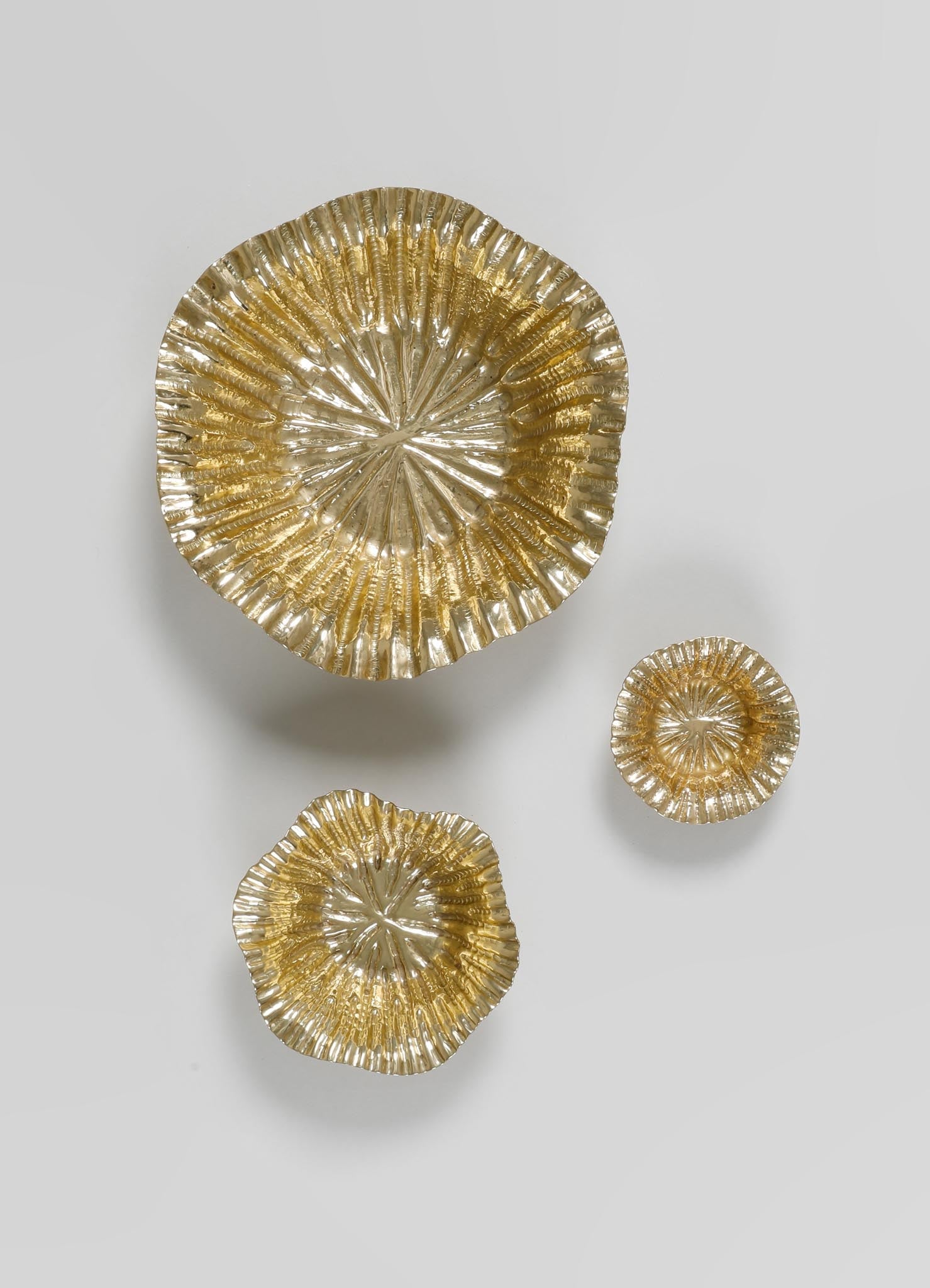 Set of three metallic gold bowls with a textured, ribbed surface and scalloped edges, made of glass or metal, featuring a reflective finish. The bowls vary in size and are arranged on a plain light background, emphasizing their contemporary and decorative style.