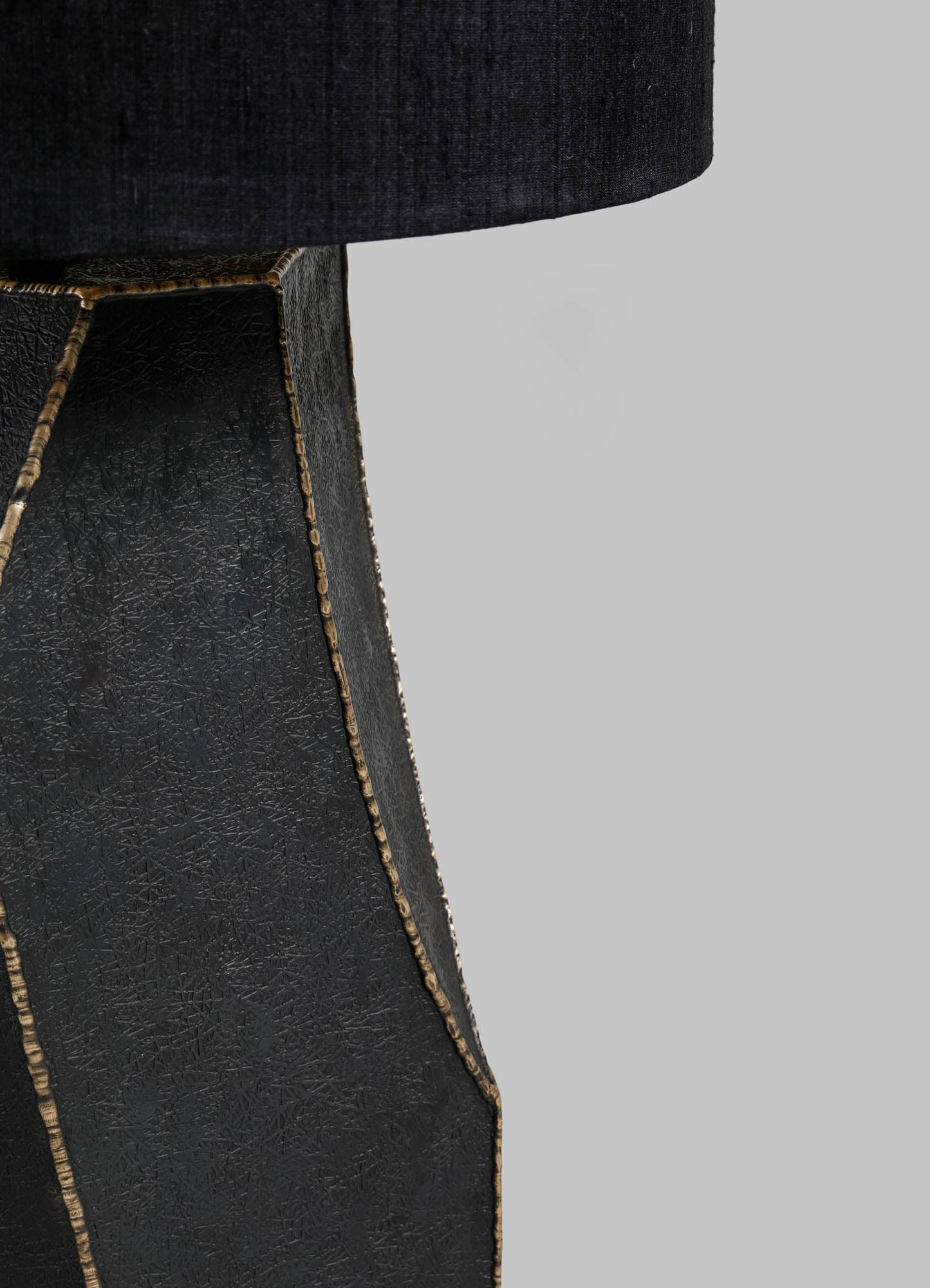 Close-up of a black leather table leg with a textured surface and metallic gold trim, part of a furniture piece with a fabric-covered top in dark fabric.