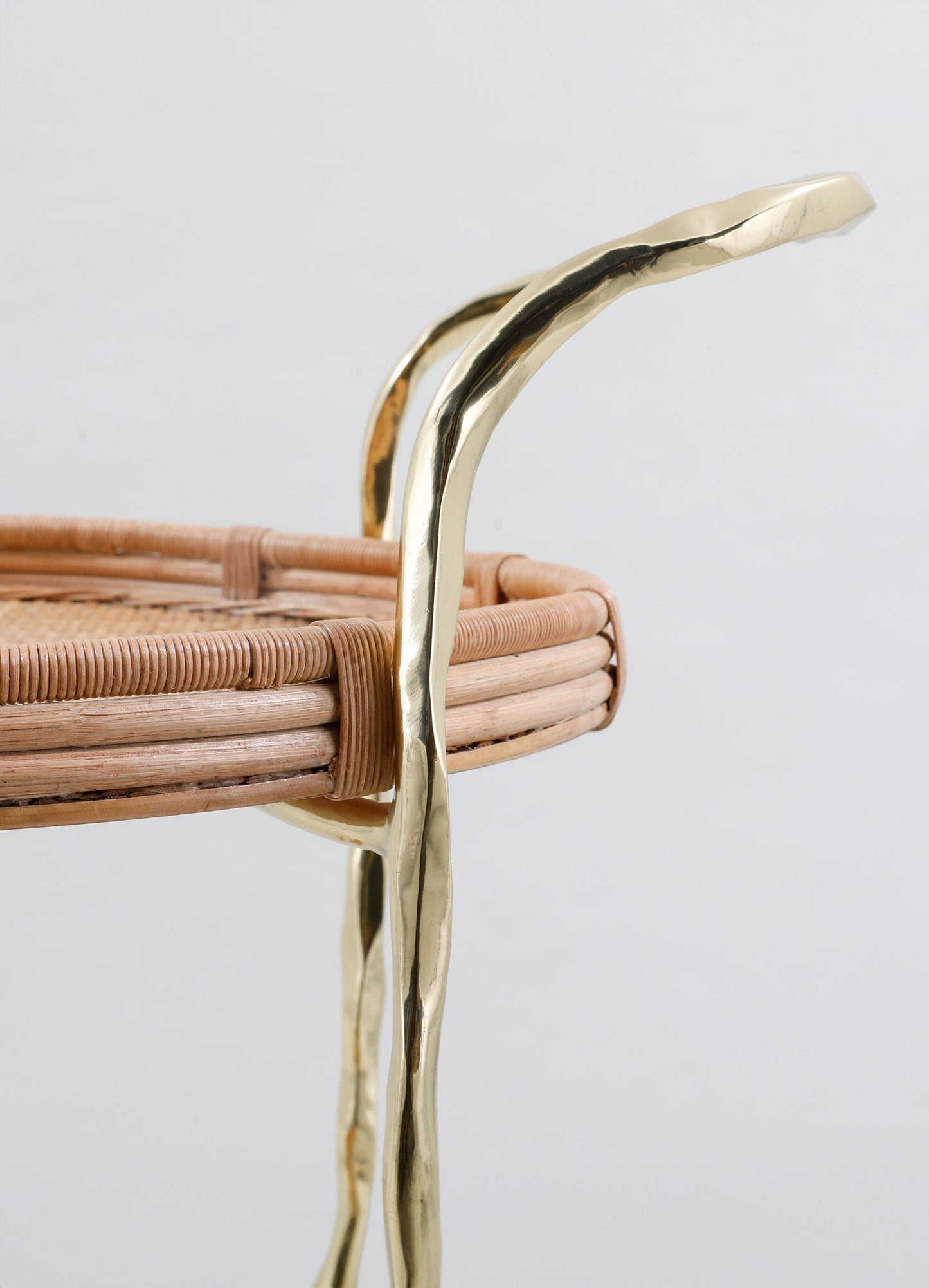 Close-up of a woven rattan basket with brass handles featuring an irregular, organic shape, showcasing a rustic and contemporary design with natural materials and metallic accents.