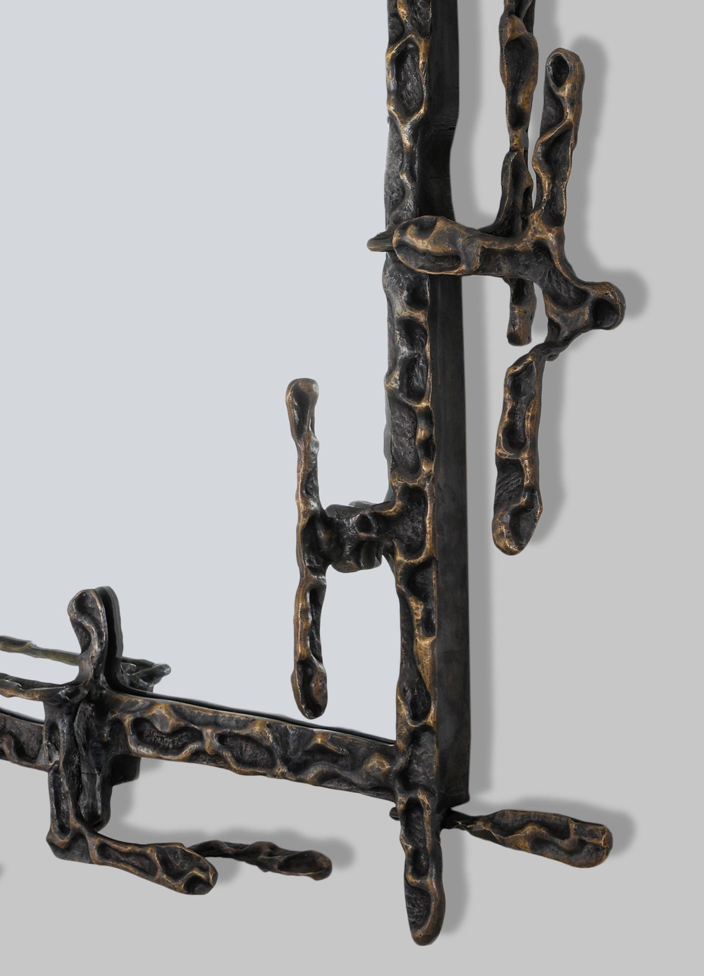 A close-up of a sculptural wall art piece with an organic, irregular shape crafted from dark metal with bronze accents, featuring a textured, abstract motif. The piece has a contemporary style with a rustic, handcrafted appearance.