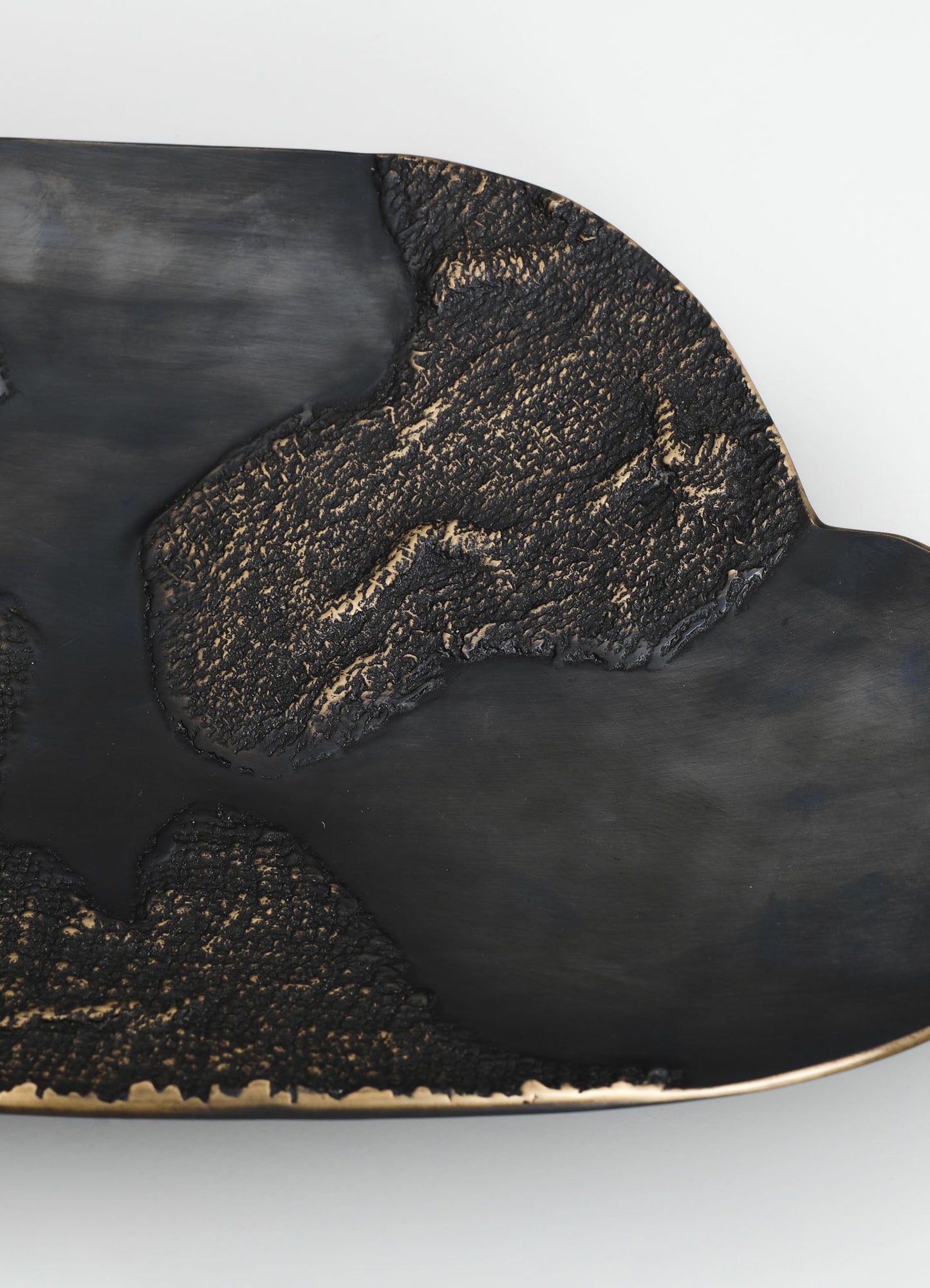 A decorative black ceramic plate with a textured, matte surface and a gold-toned rim, featuring an abstract, flowing design pattern. The plate has an irregular shape with organic, curving edges.