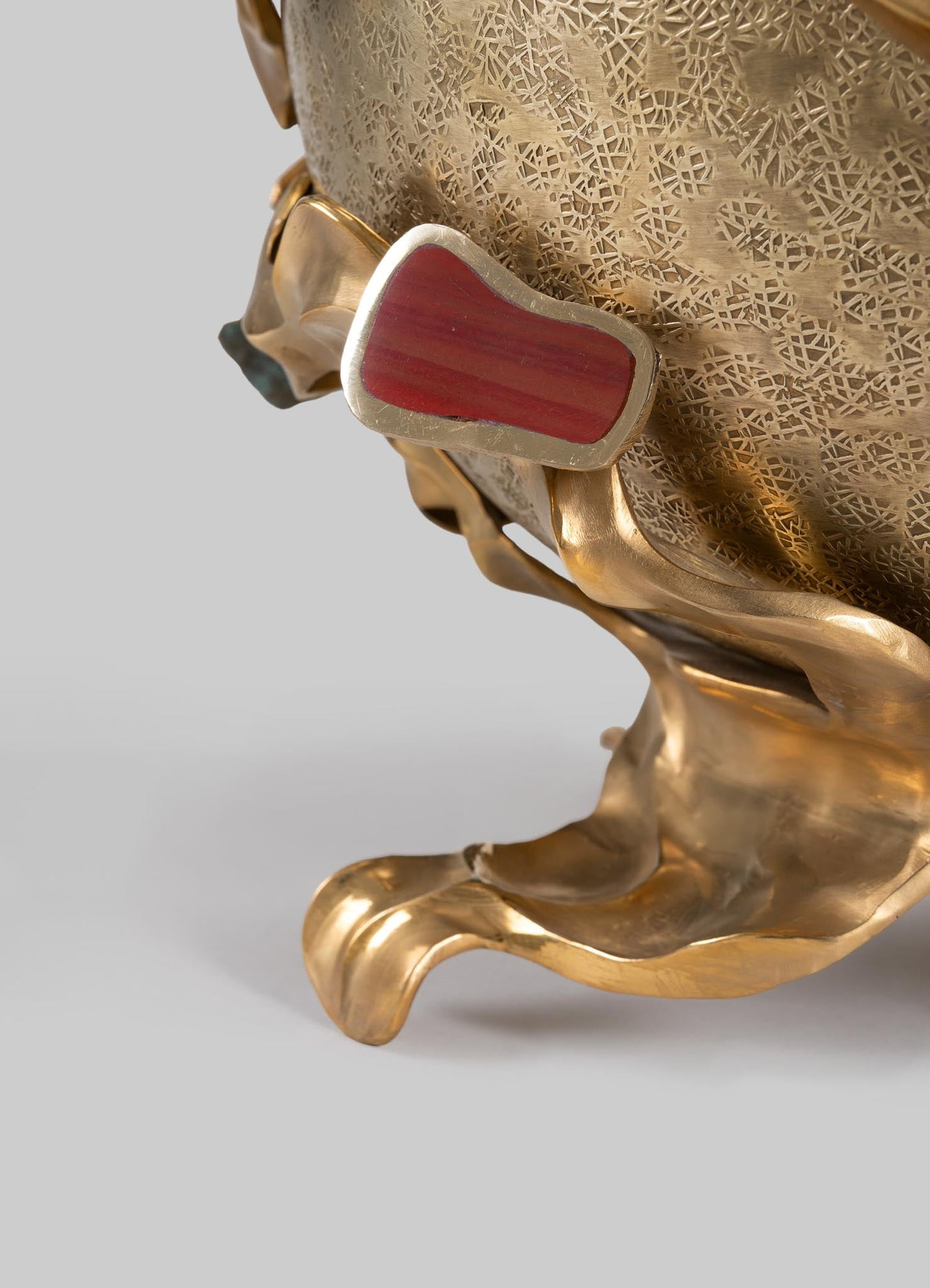 Gold-plated jewelry with a bold red stone, featuring organic-shaped design elements and a polished finish.