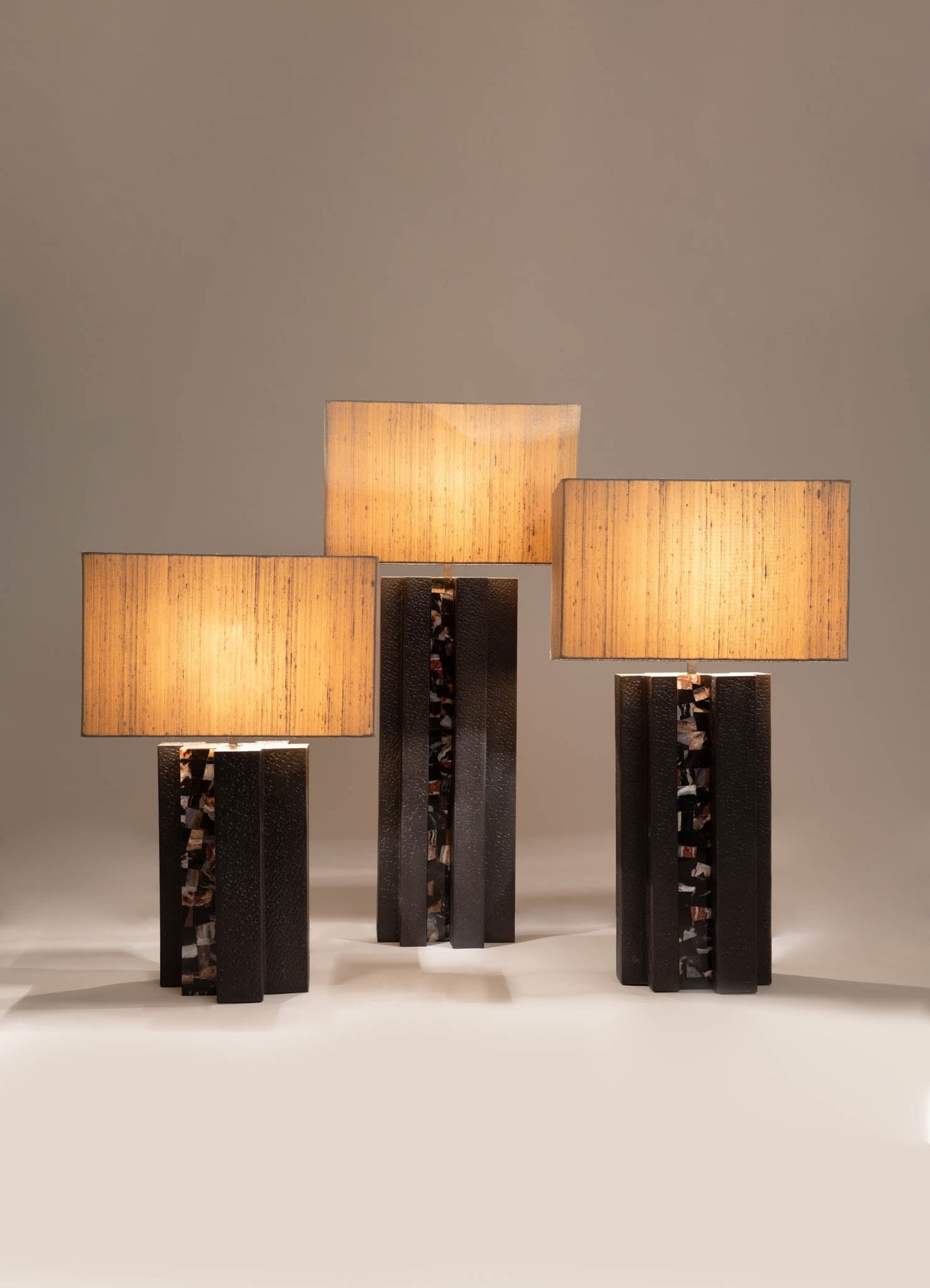 Glass table lamps with rectangular beige fabric shades, featuring dark sculptural bases with textured and patterned accents, in a contemporary style.