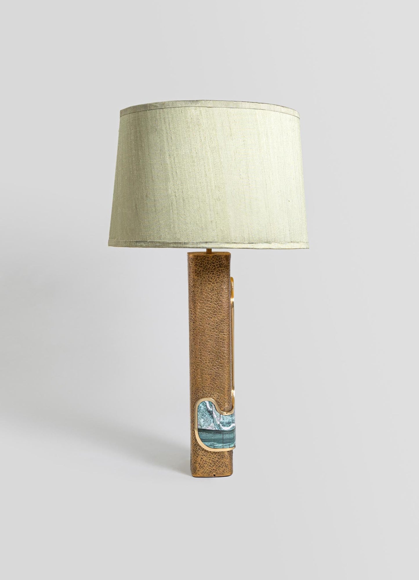 A table lamp with a textured, gold-toned ceramic base featuring a blue and white marble inlay patch, topped with a cream-colored fabric drum shade.