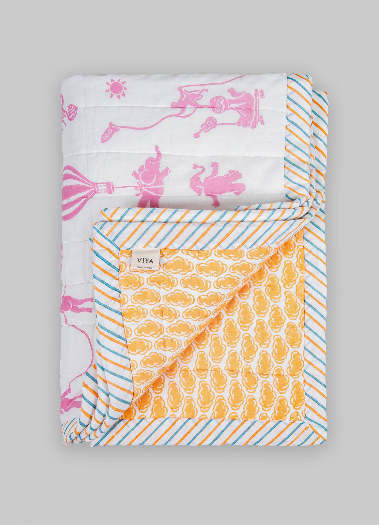 Colorful, reversible quilt with printed patterns on cotton fabric, featuring pink animal and floral motifs on one side and orange cloud motifs on the other, edged with striped binding in blue, orange, and white.