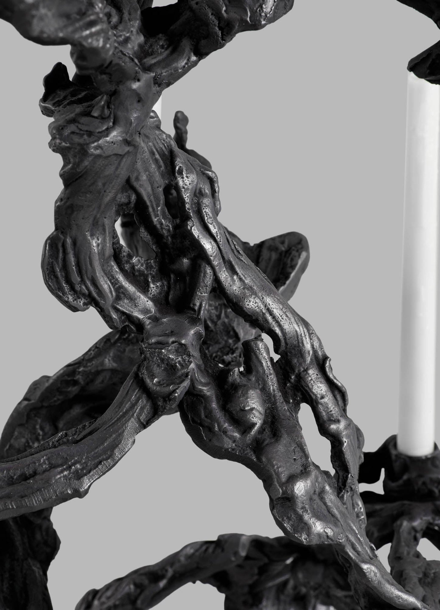 A close-up of a black decorative sculpture with a textured, organic form resembling intertwined natural elements, made from a glossy material. The background is neutral gray, highlighting the intricate, flowing shapes of the piece.