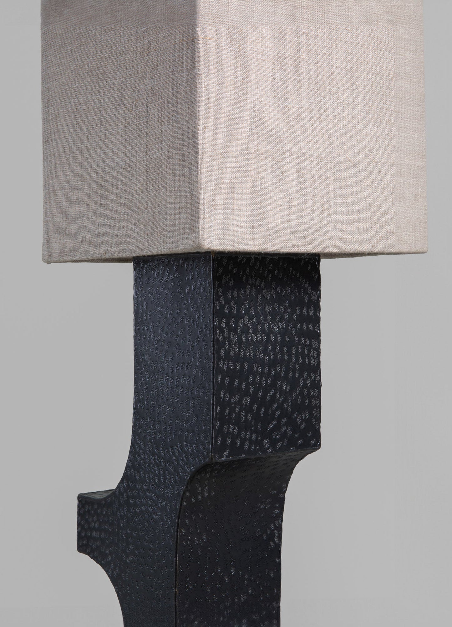 Close-up of a table lamp featuring a black textured ceramic base with a leather-like pattern and a rectangular beige fabric lampshade, creating a contemporary and sophisticated style.