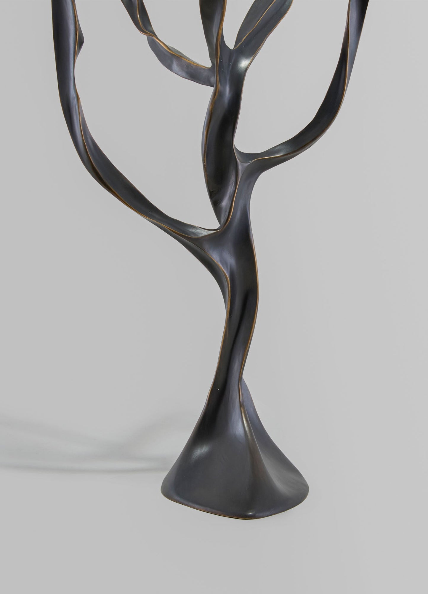 A sculptural table centerpiece or decorative object made of black metal with gold accents, featuring twisted, organic lines and a smooth, polished surface.