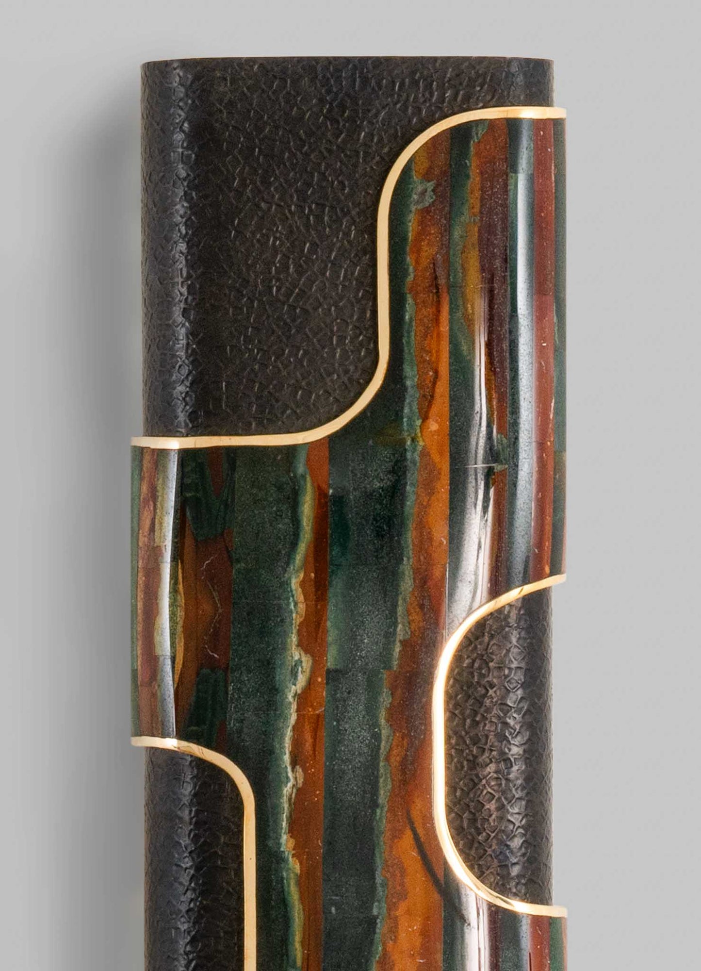 Decorative cylindrical sculpture combining textured black material with colorful, marble-like inlays in shades of green, orange, and brown, accented with gold trim. The style is contemporary with abstract geometric motifs, creating a striking visual contrast.