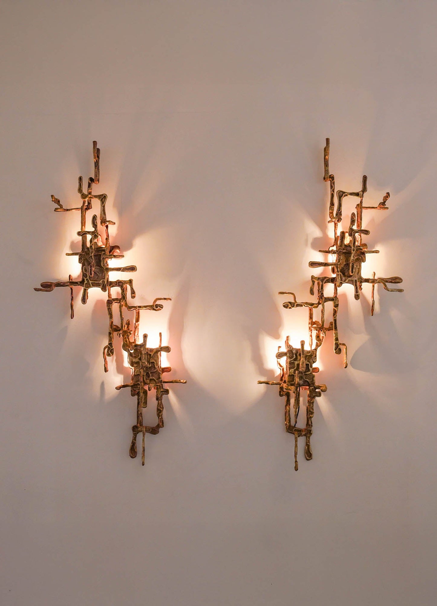 Pair of modern wall sconces made of twisted brass with a sculptural, organic form, featuring integrated light sources that cast soft shadows on a neutral wall.