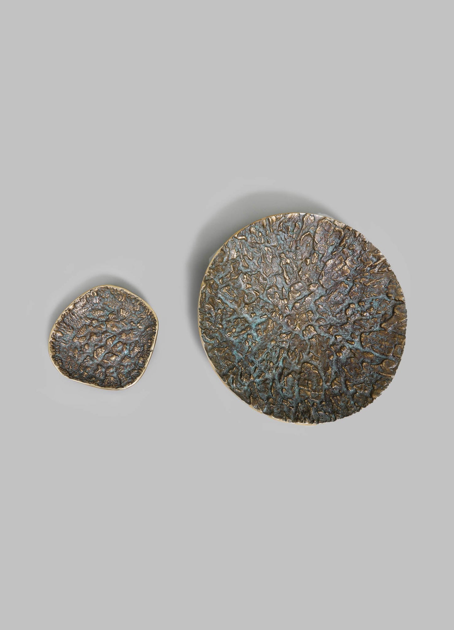 Decorative metal plates with textured, organic surface patterns in dark bronze and gold accents, set against a light gray background.