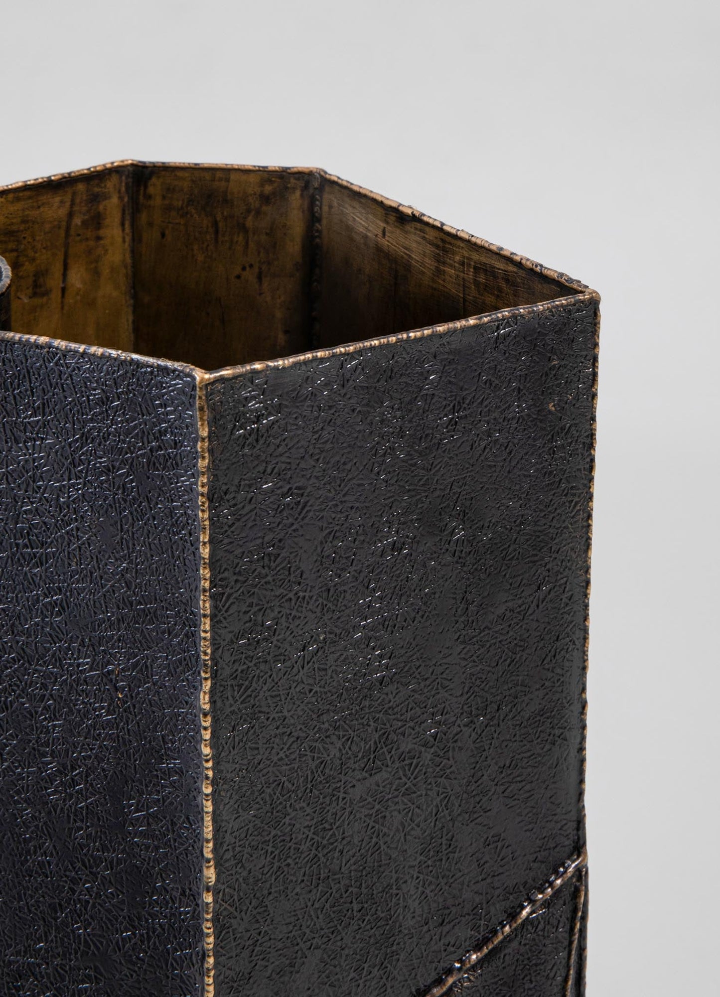 A black ceramic vase with a textured, crackled surface and a matte finish, featuring an angular, geometric shape with a gold-tone rim.