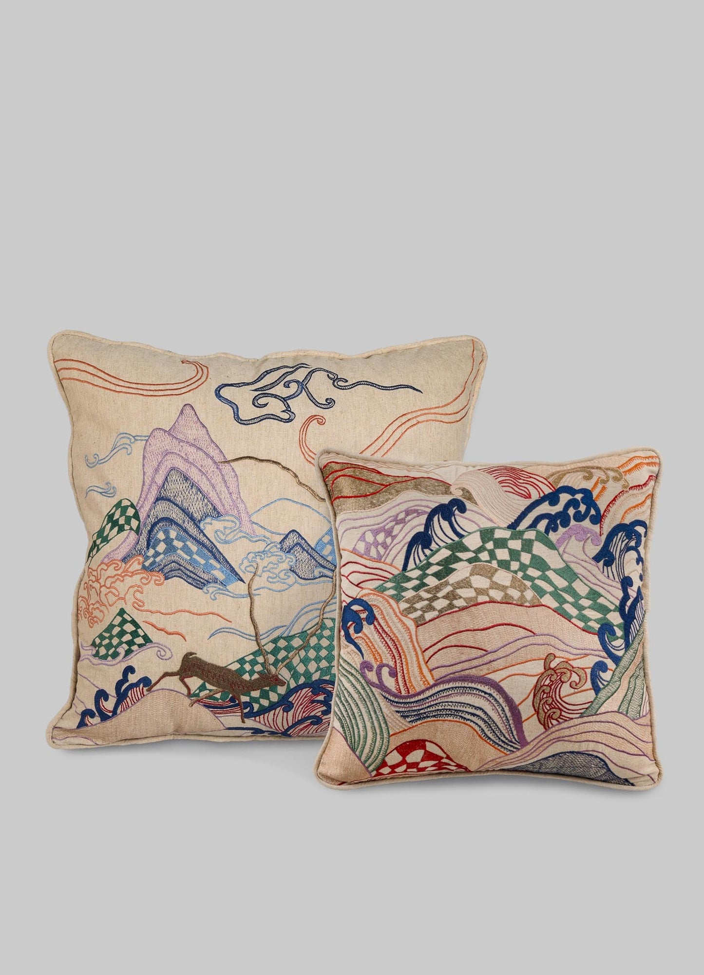 Embroidered decorative cushions with mountain and wave motifs, featuring colorful thread embroidery in shades of purple, blue, red, green, and beige on a neutral fabric background.