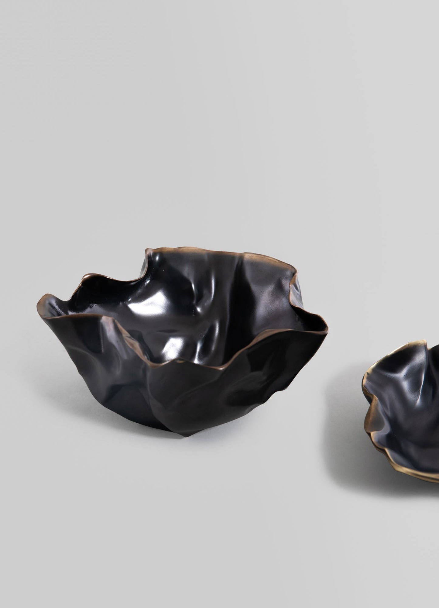 Black ceramic bowls with organic, irregular shapes and a glossy finish, featuring subtle gold accents along the wavy edges. The design combines contemporary and artisanal styles with smooth, flowing lines.